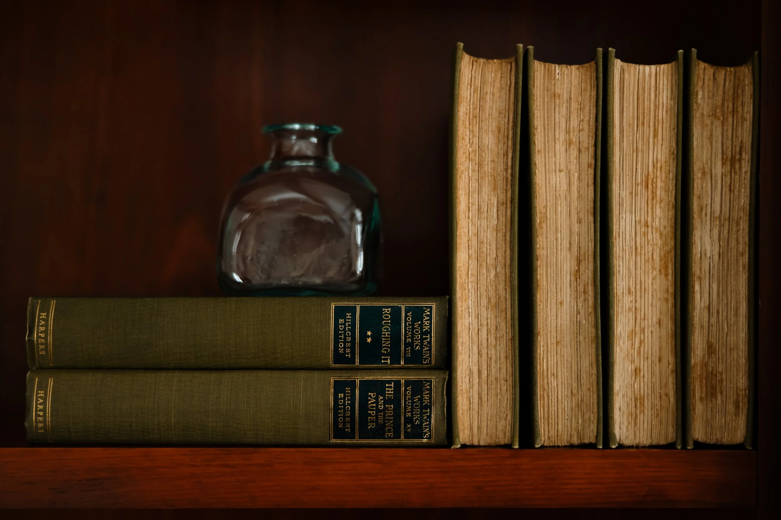 Close-up of vintage books and glass vessel styled on wood shelving.