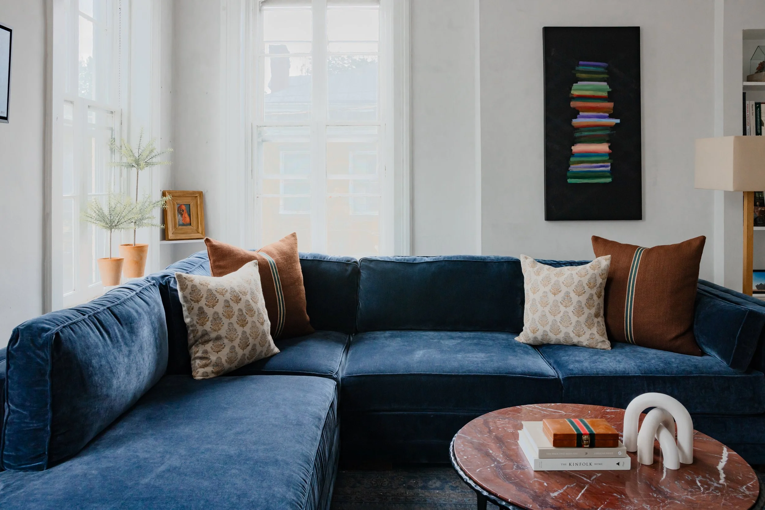 Blue sectional sofa with layered patterned pillows in a light-filled living room.