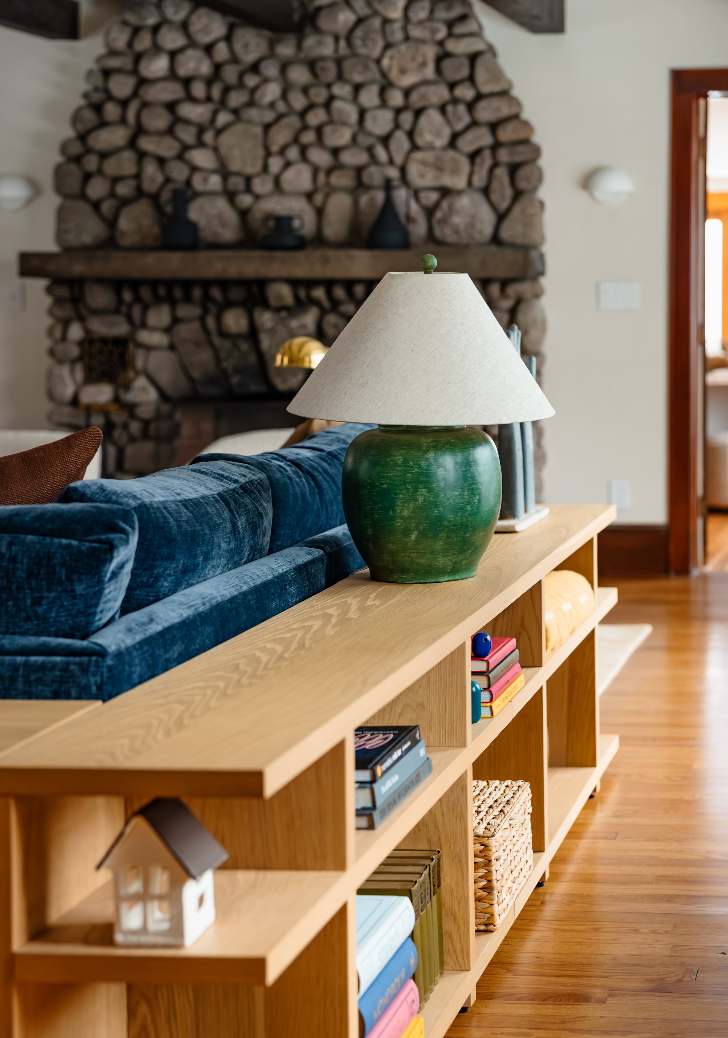 Green ceramic lamp on oak console with stone fireplace softly blurred in the background.