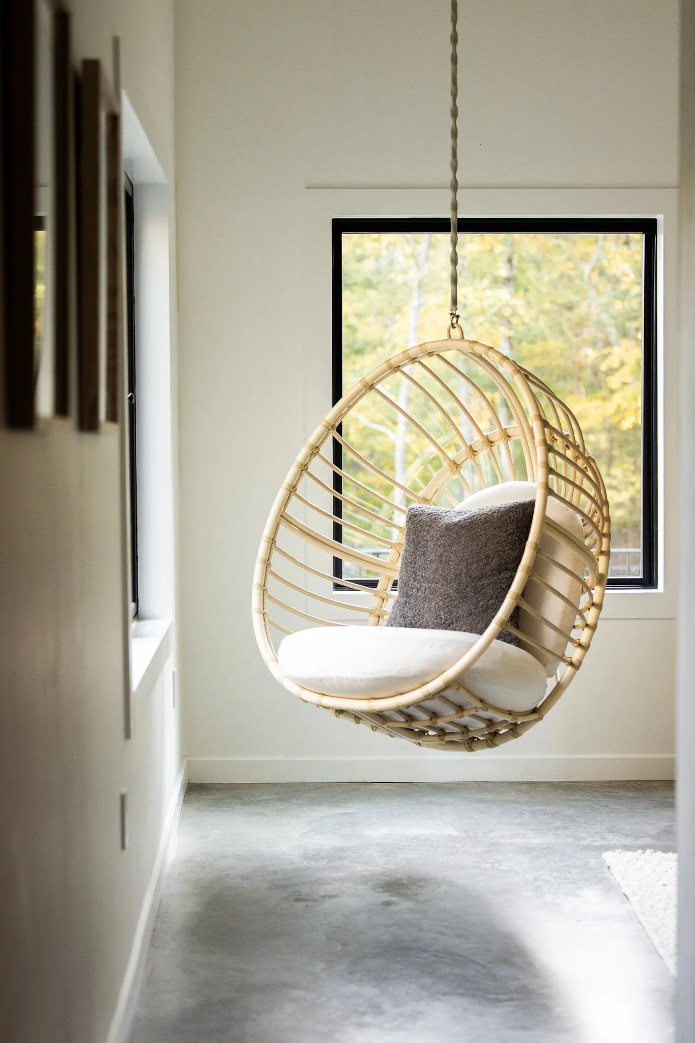 Hanging rattan chair suspended in a bright bedroom with large window views.