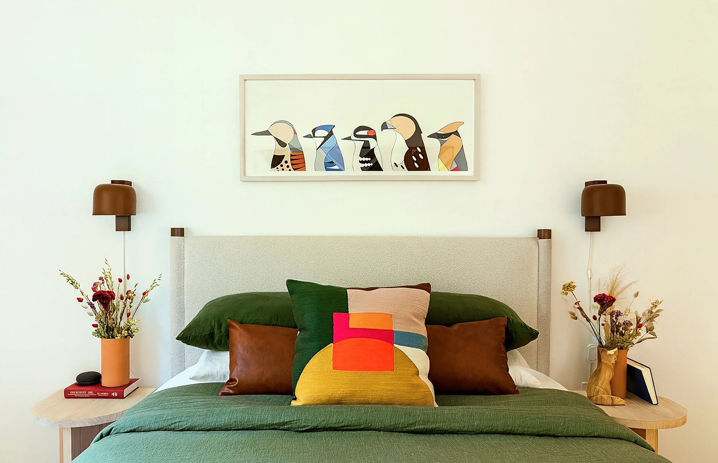 Bedroom with upholstered headboard, layered green bedding, and framed artwork above.