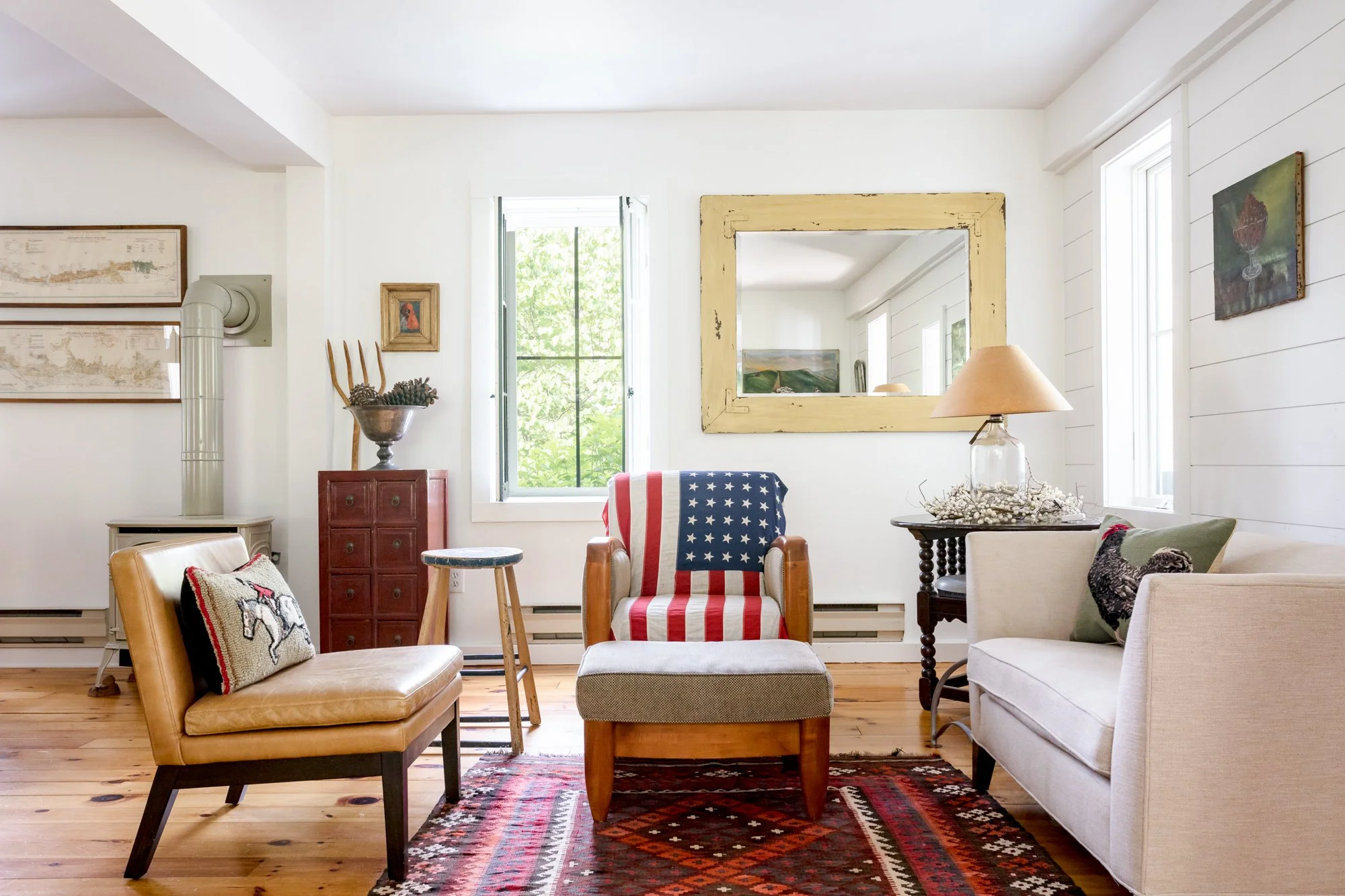 Cozy sitting area with vintage furniture, american flag detail, wood stove, and patterned rug.