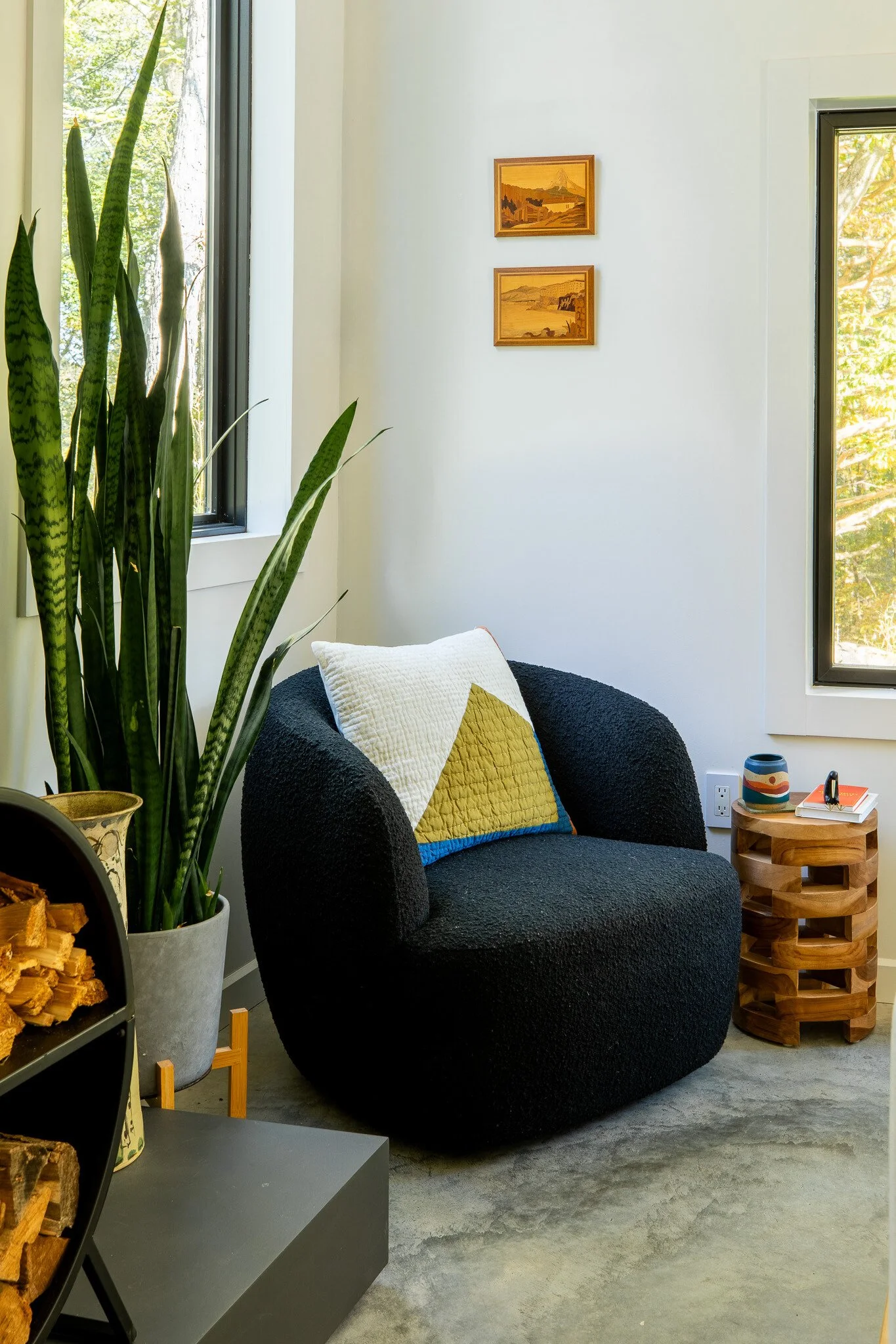 Cozy reading nook with black lounge chair, tall plant, and window overlooking trees.