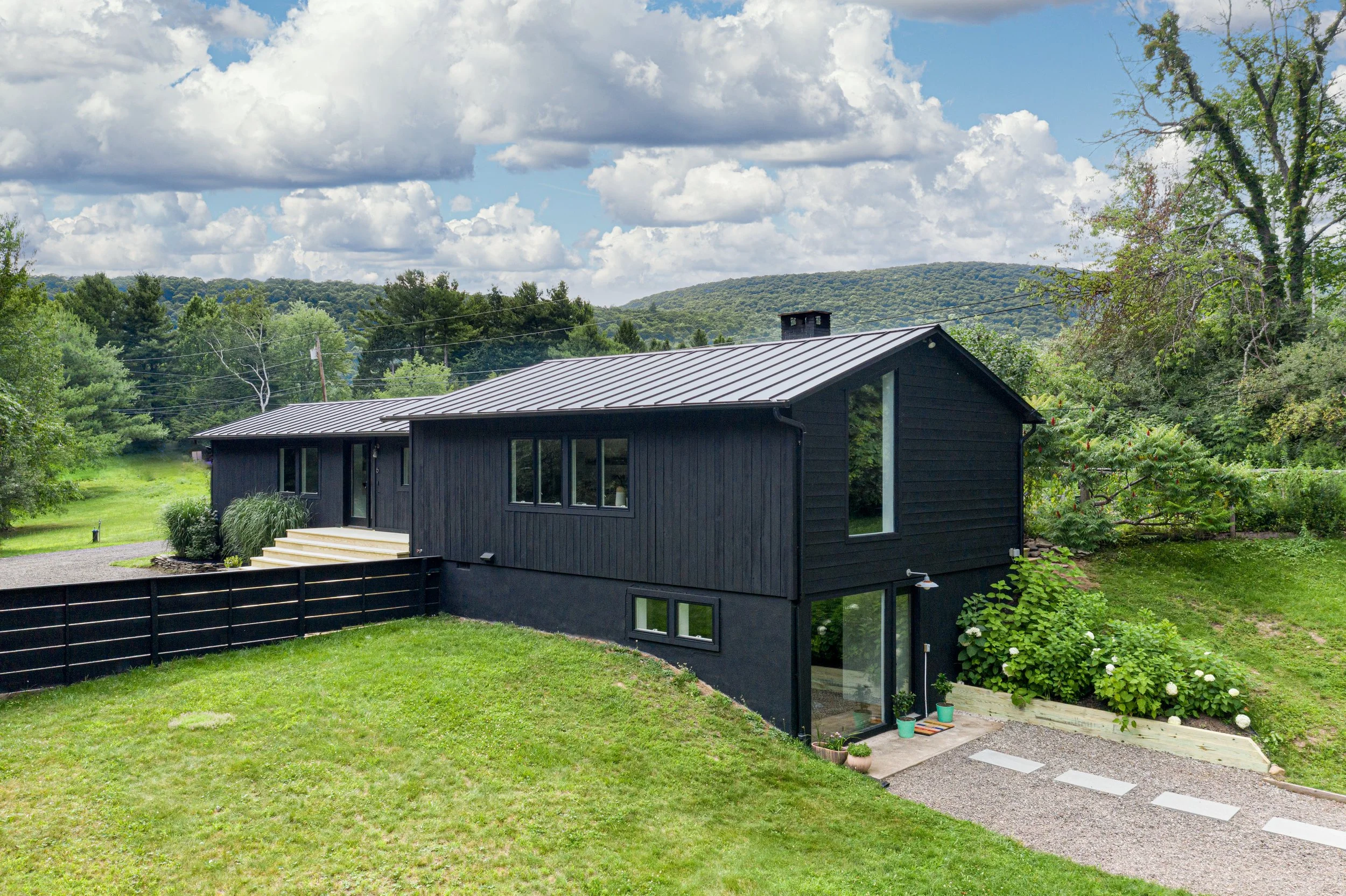 Black modern farmhouse exterior with metal roof set against rolling green hills.