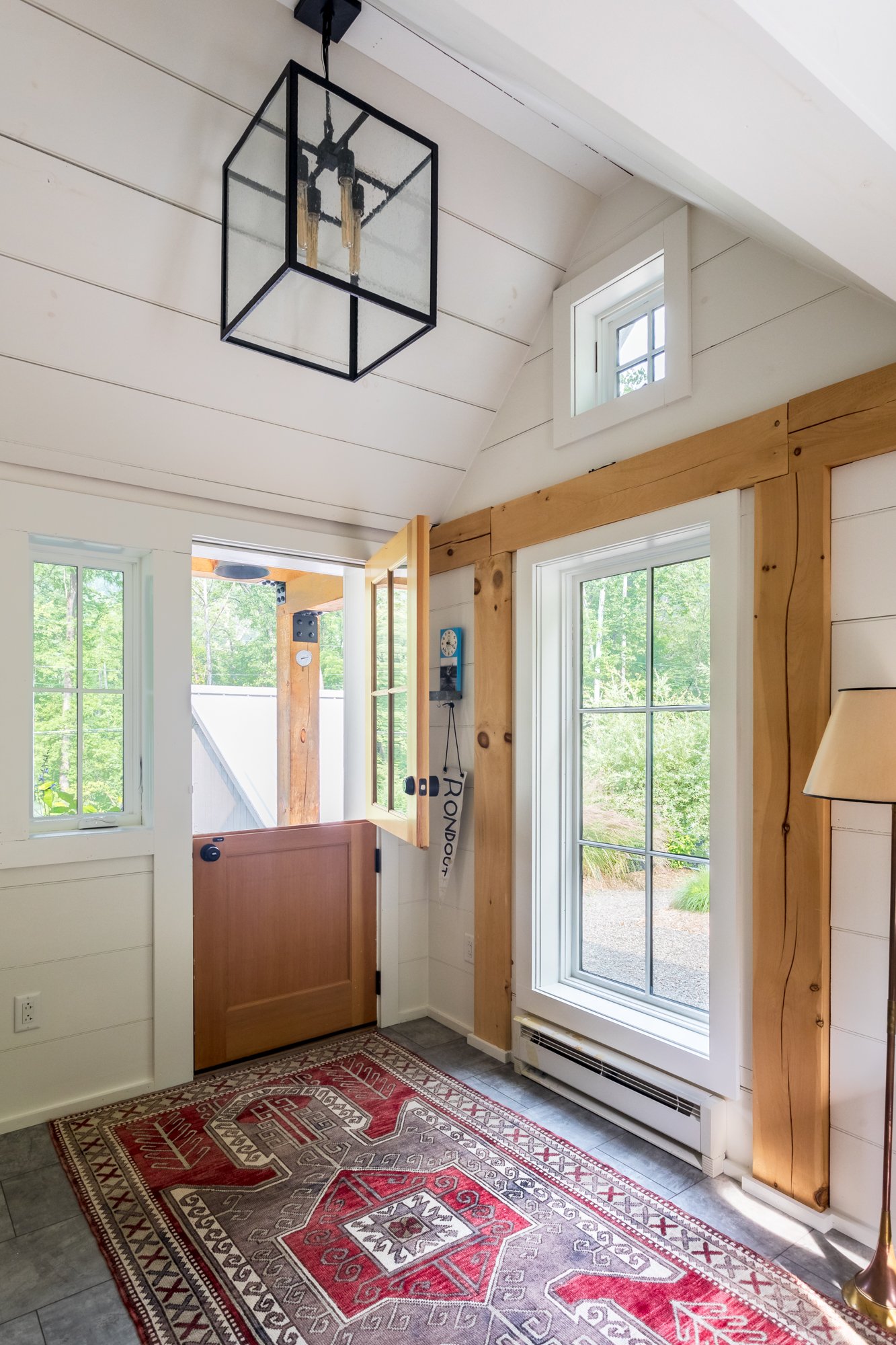 Cottage entryway with half glass door, natural wood trim, and red patterned rug.