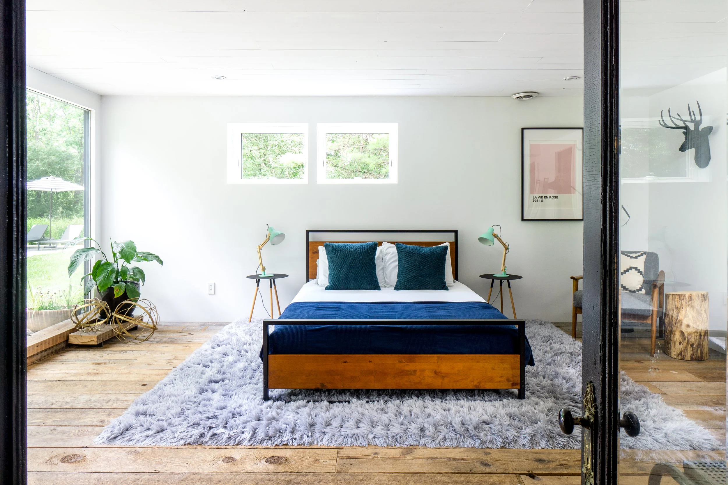 Guest bedroom with wood floors, plush gray rug, and modern wood and black metal bed frame.