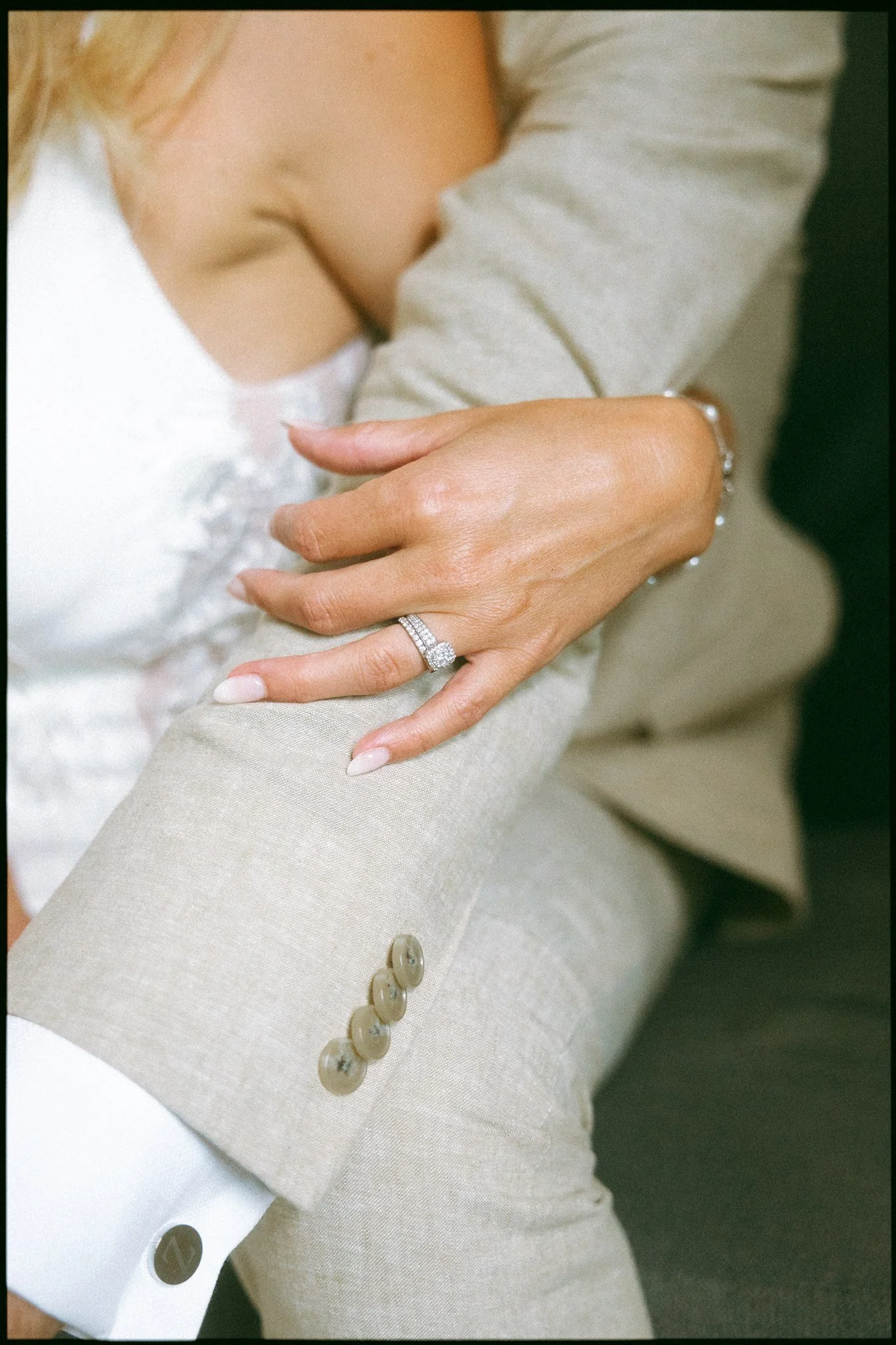 Main d’une femme portant une bague de fiançailles, posée sur le bras d’une personne habillée d’un costume beige, captée par un Photographe mariage Québec à Charlevoix.
