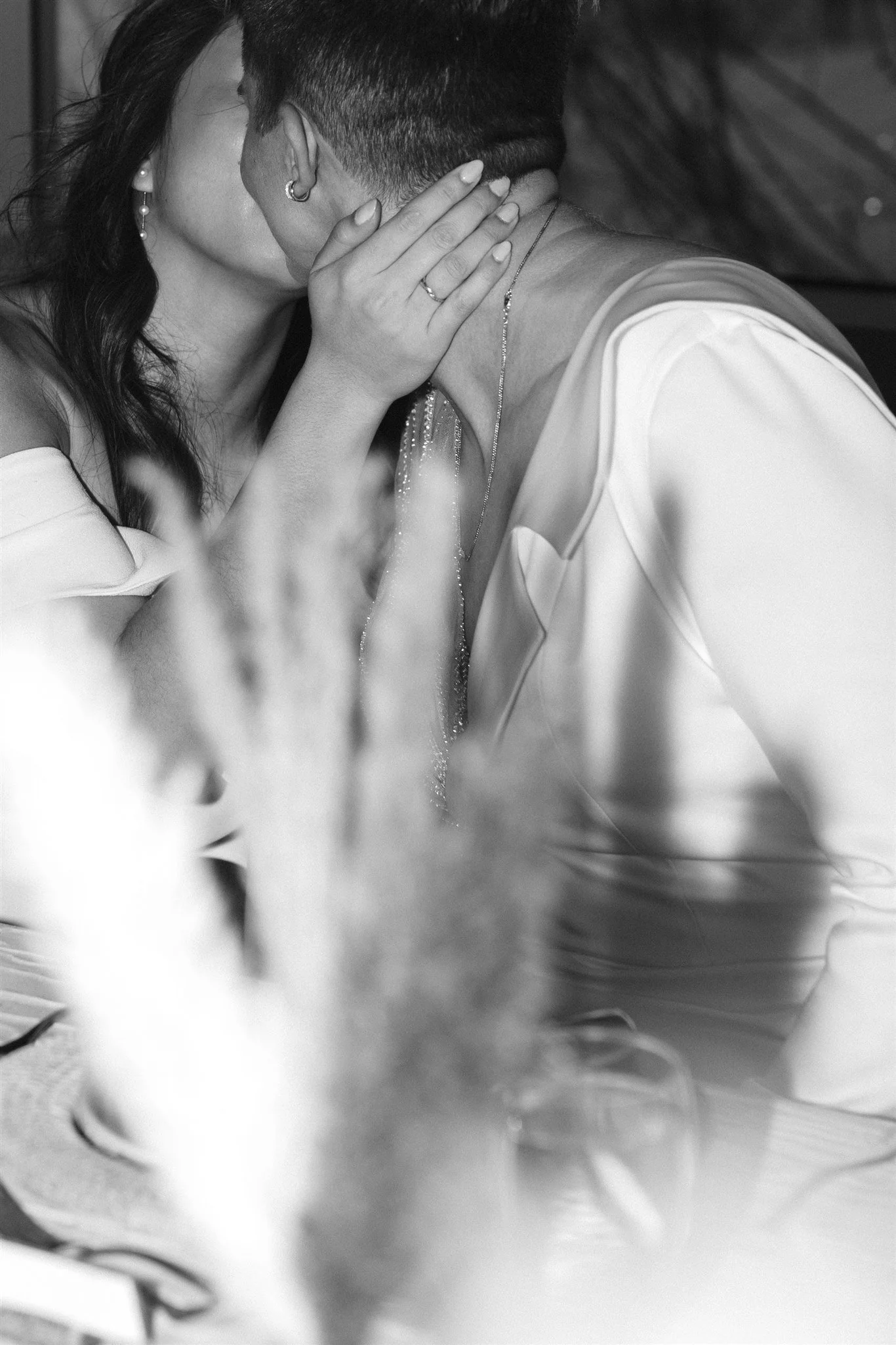 Une photo en noir et blanc montrant deux personnes qui semblent s'embrasser ou partager un moment intime, avec une mise au point sur leurs visages, leurs mains et leurs épaules.