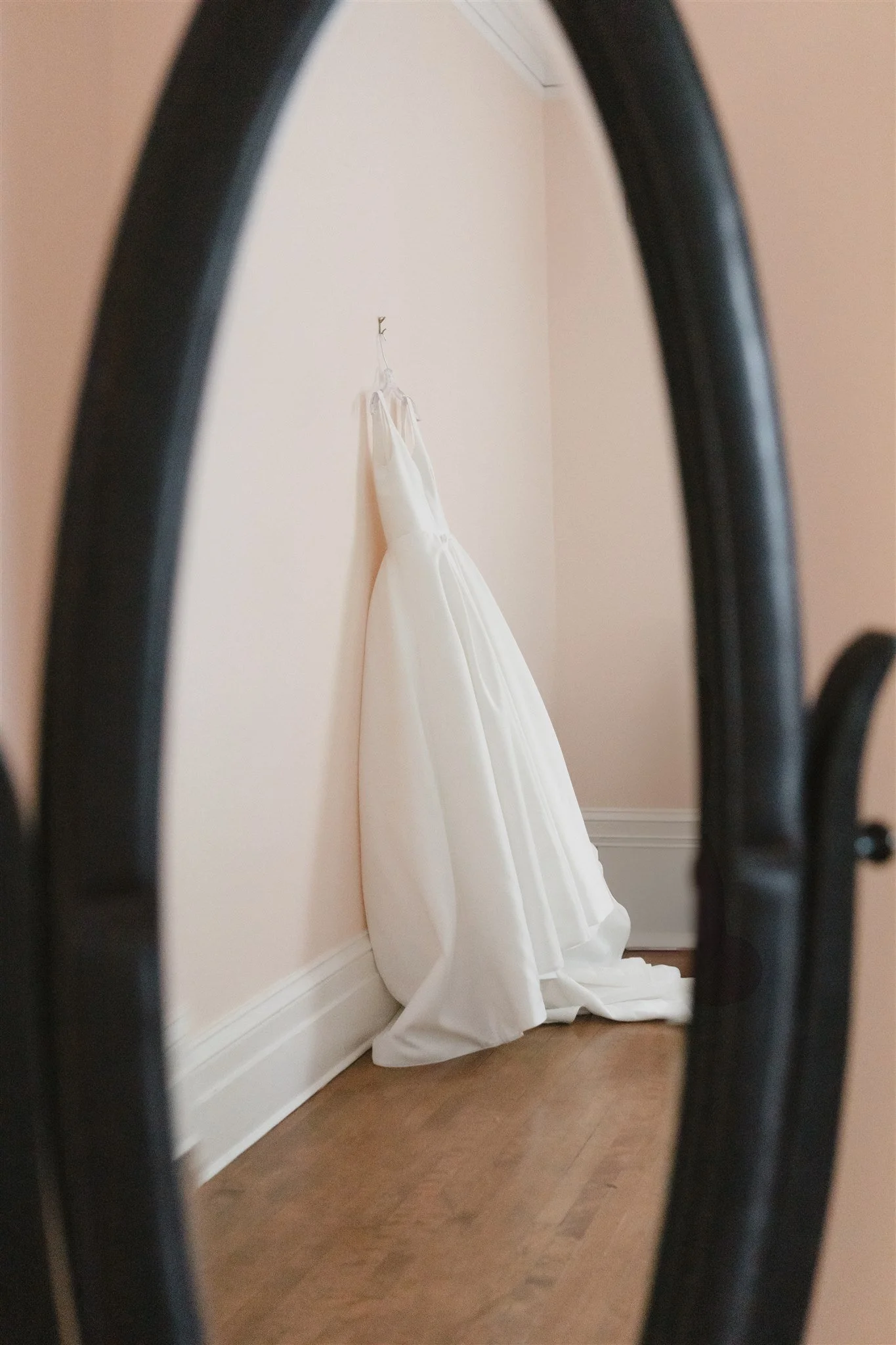 Une robe de mariage blanche suspendue contre un mur dans une pièce, vue à travers un miroir courbé.