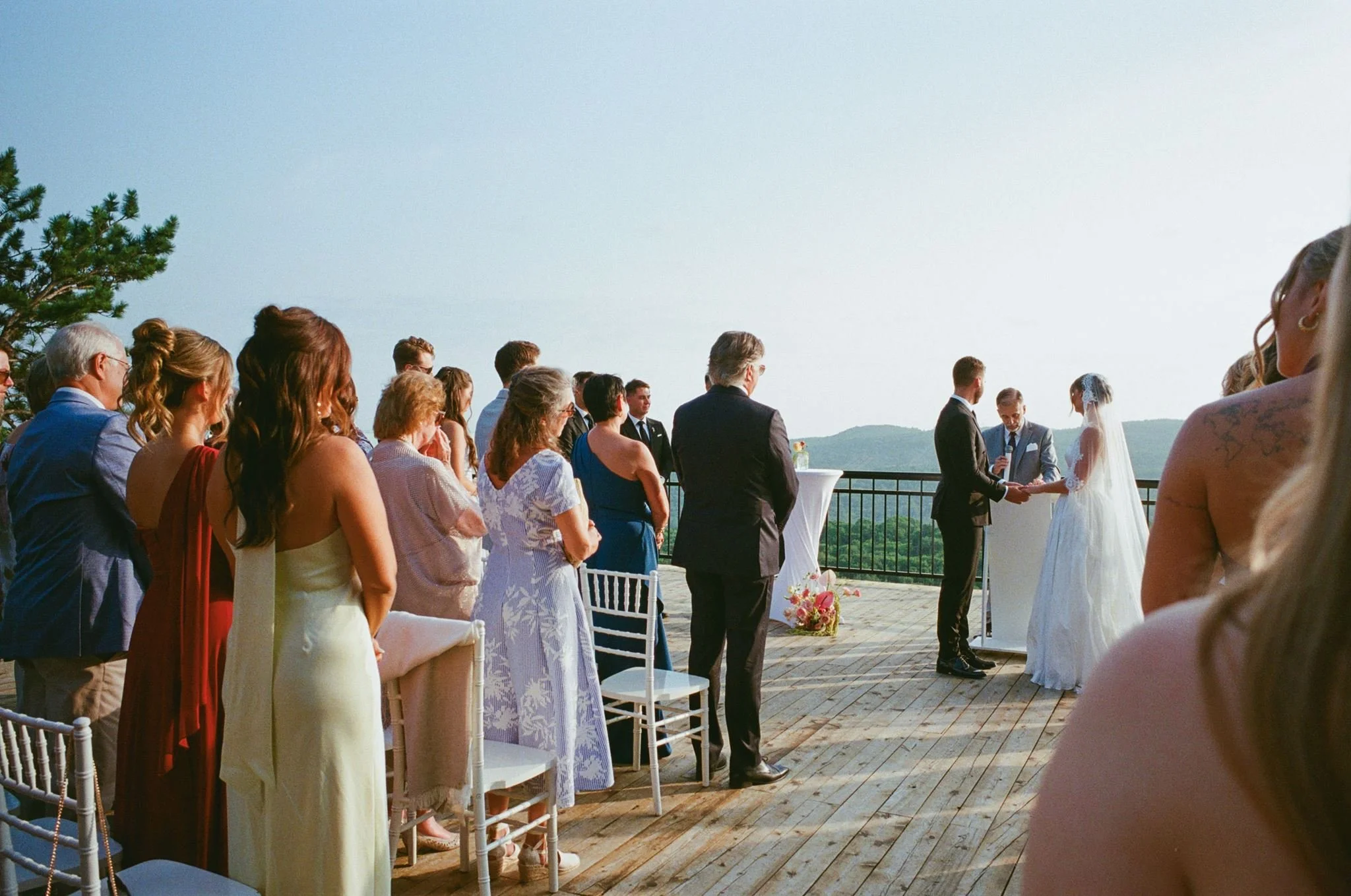Cérémonie de mariage en plein air avec des invités alignés et un couple de mariés échangeant leurs vœux sur une terrasse avec vue panoramique.