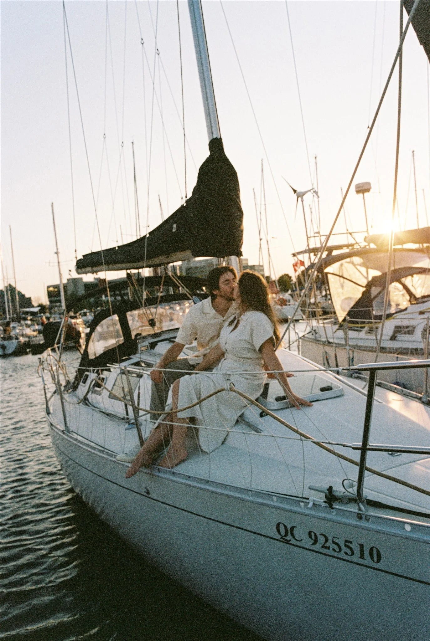 Couple assis sur le pont d’un voilier au coucher du soleil, avec plusieurs bateaux dans le port en arrière-plan, captés par un Photographe mariage Québec à la Marina de Québec.