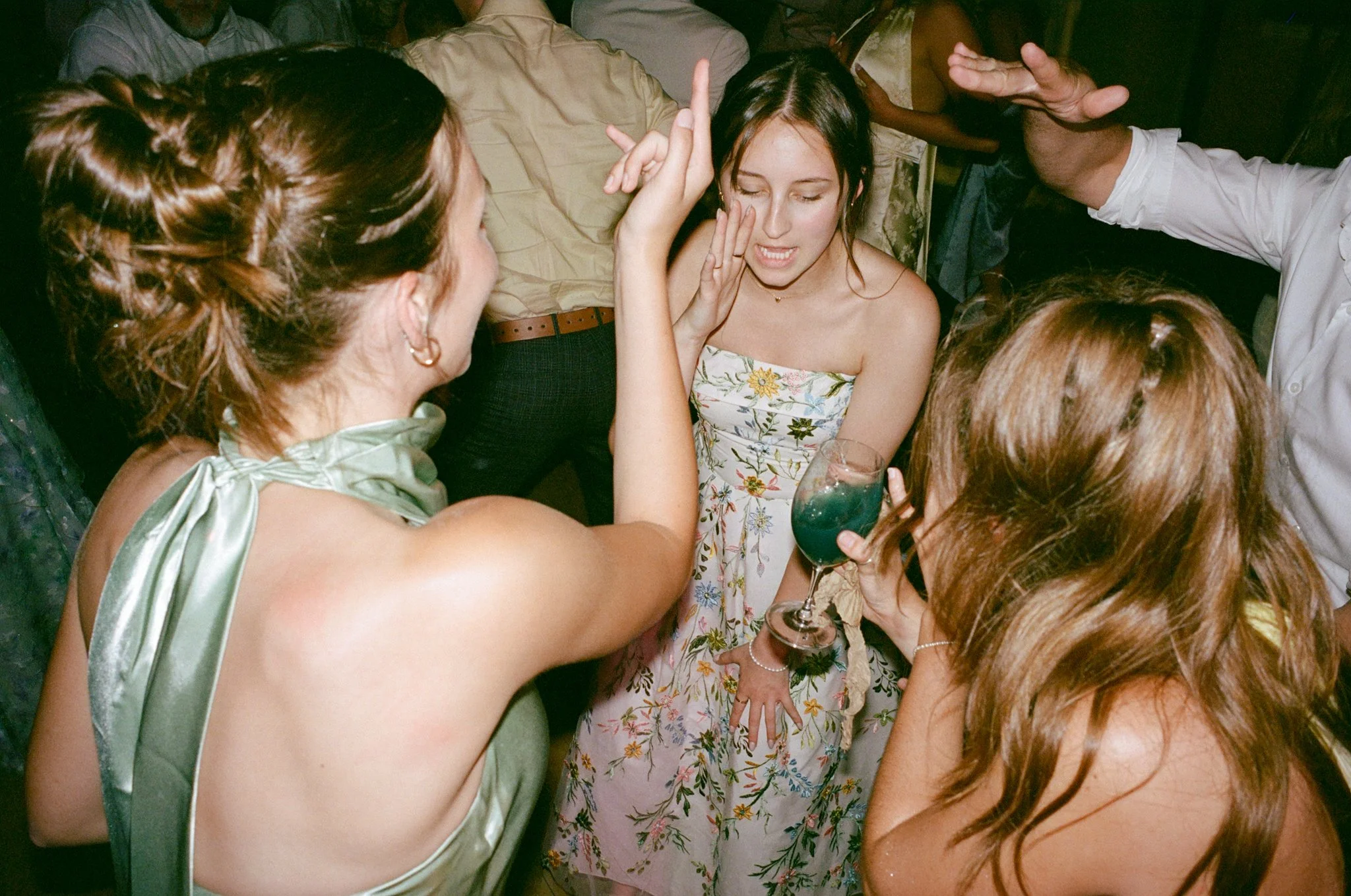 Groupe de jeunes filles et jeunes femmes à une fête, certaines tenant un verre, en discuter et rire dans une ambiance festive.