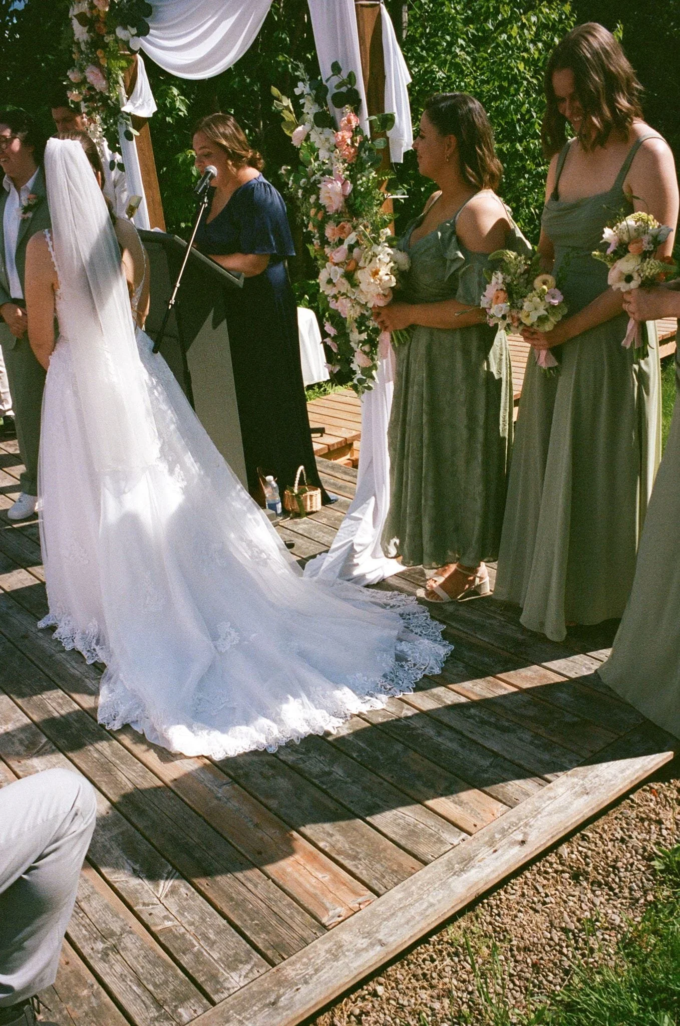 Cérémonie de mariage en extérieur avec la mariée en robe blanche, demoiselles d'honneur en robes vertes, décor floral et invités présents.