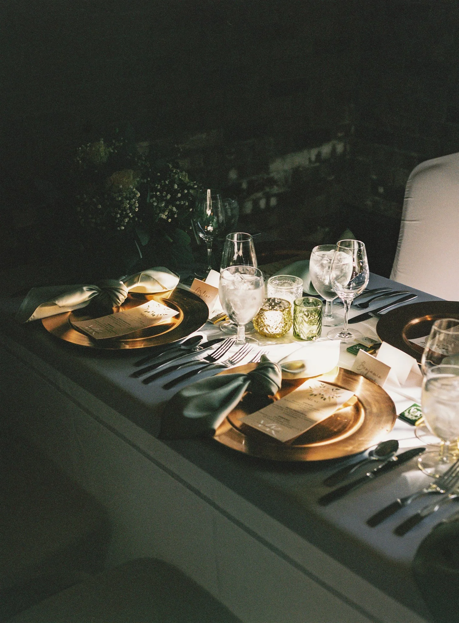 Table élégamment dressée pour un dîner avec des verres à eau, des assiettes dorées, des couverts et des menus, dans une ambiance tamisée.