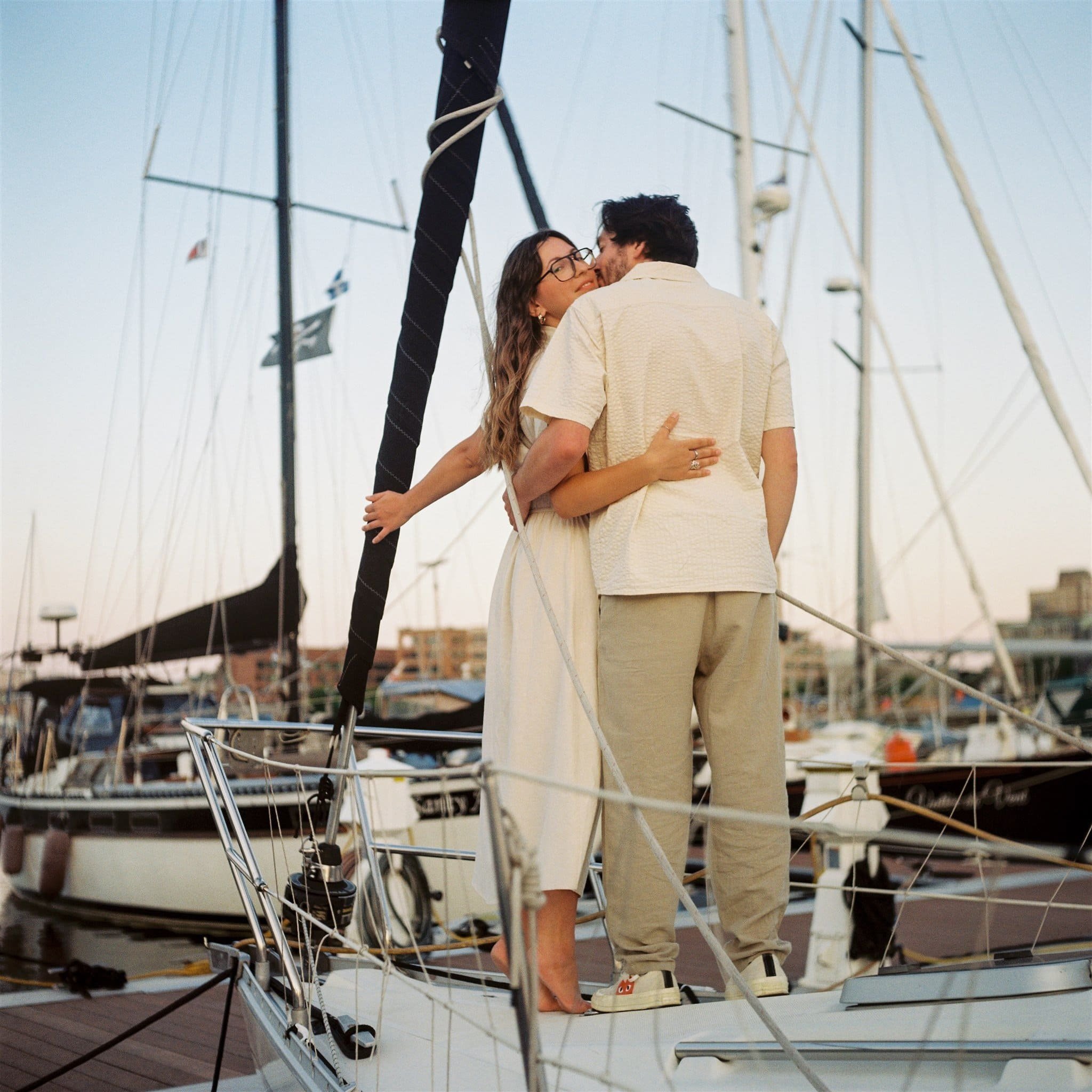 Couple s’embrassant sur un bateau dans un port au coucher du soleil, avec d’autres embarcations en arrière-plan, capté par un Photographe mariage Québec.