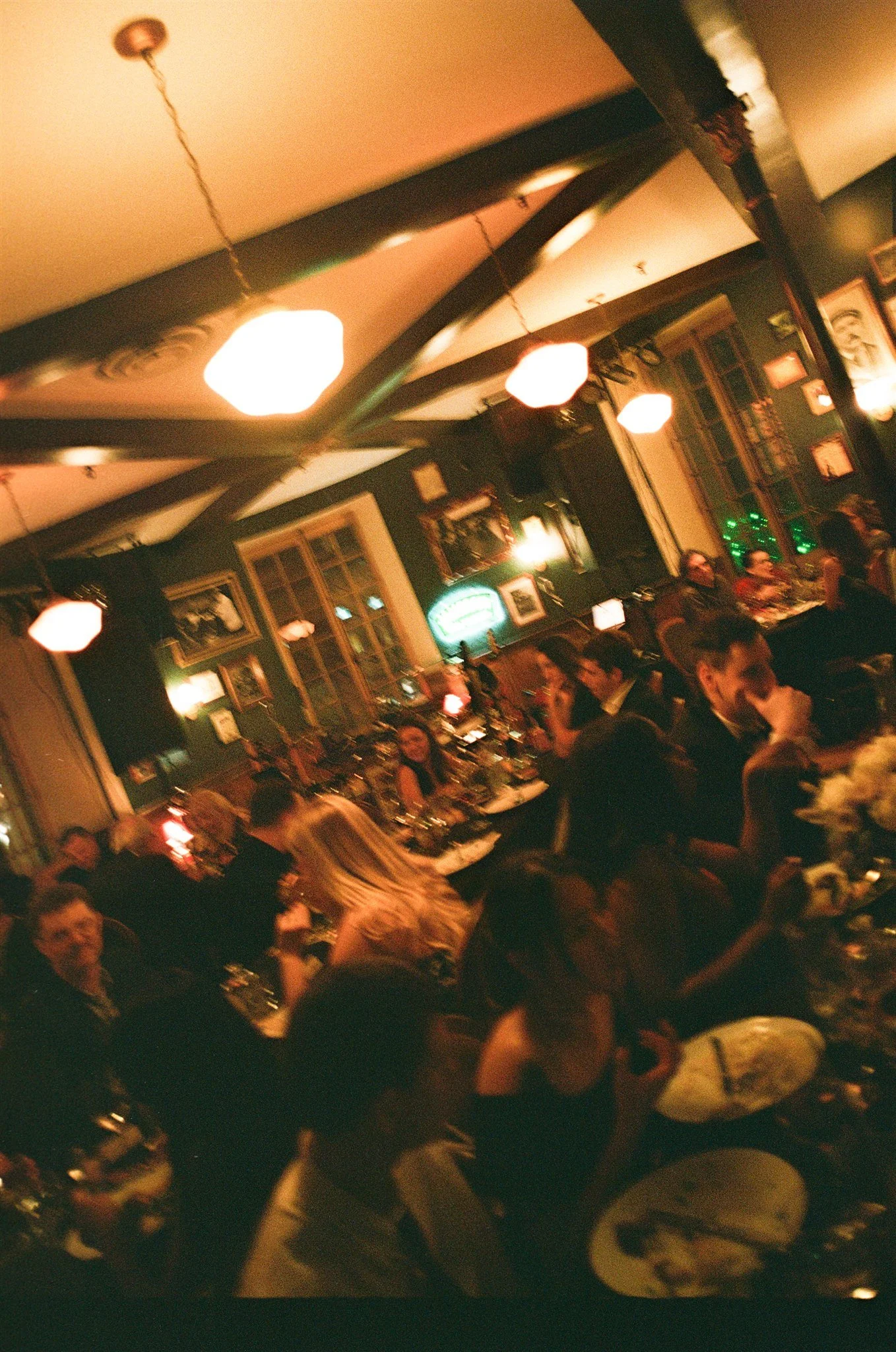 Une salle à manger animée dans un restaurant, avec des personnes assises à des tables, des lampes suspendues au plafond et des murs décorés.