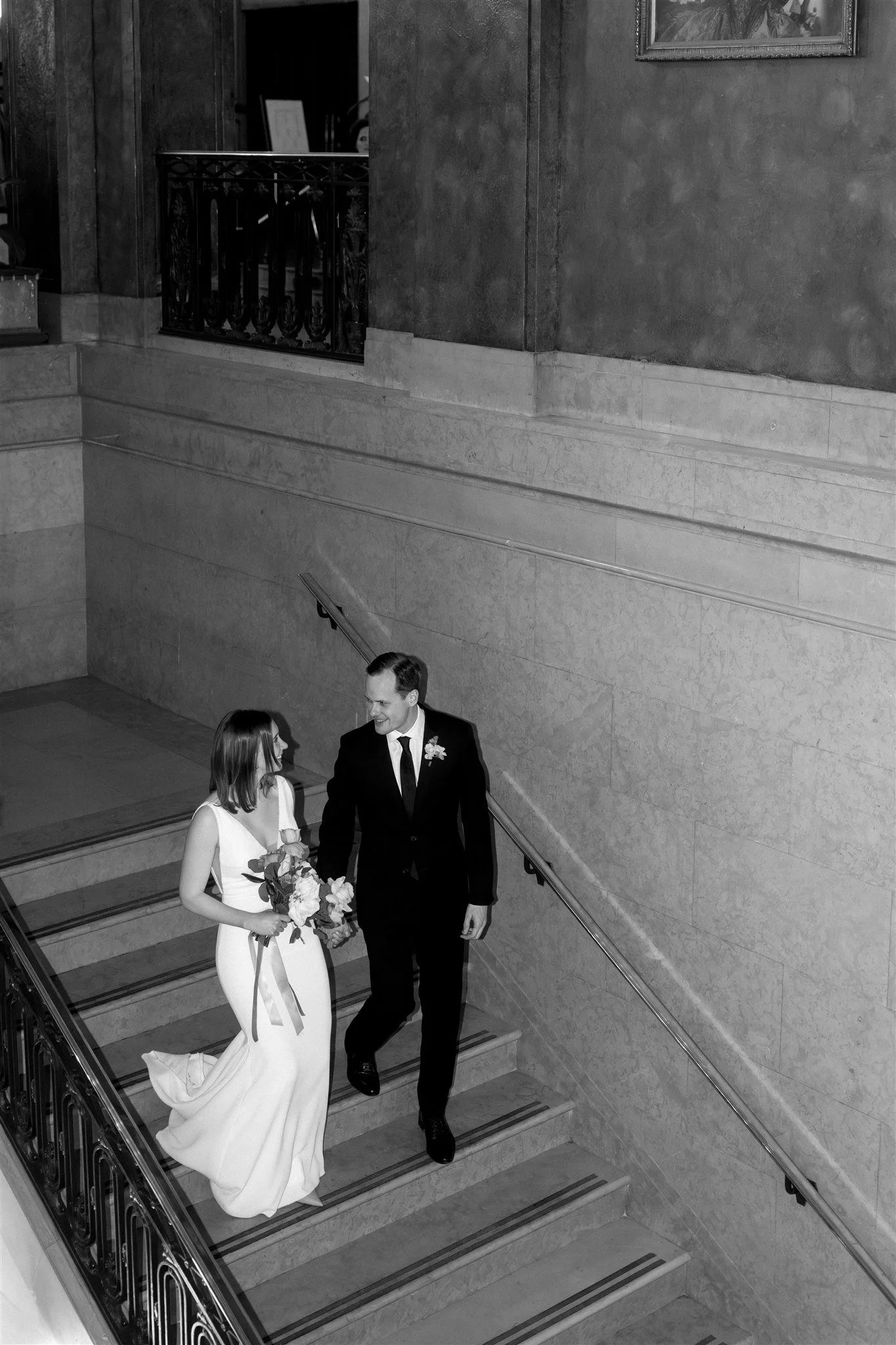 Mariée en robe blanche et marié en costume noir descendant un escalier avec une femme tenant un bouquet, captés par un Photographe mariage Québec au Fairmont Le Château Frontenac.