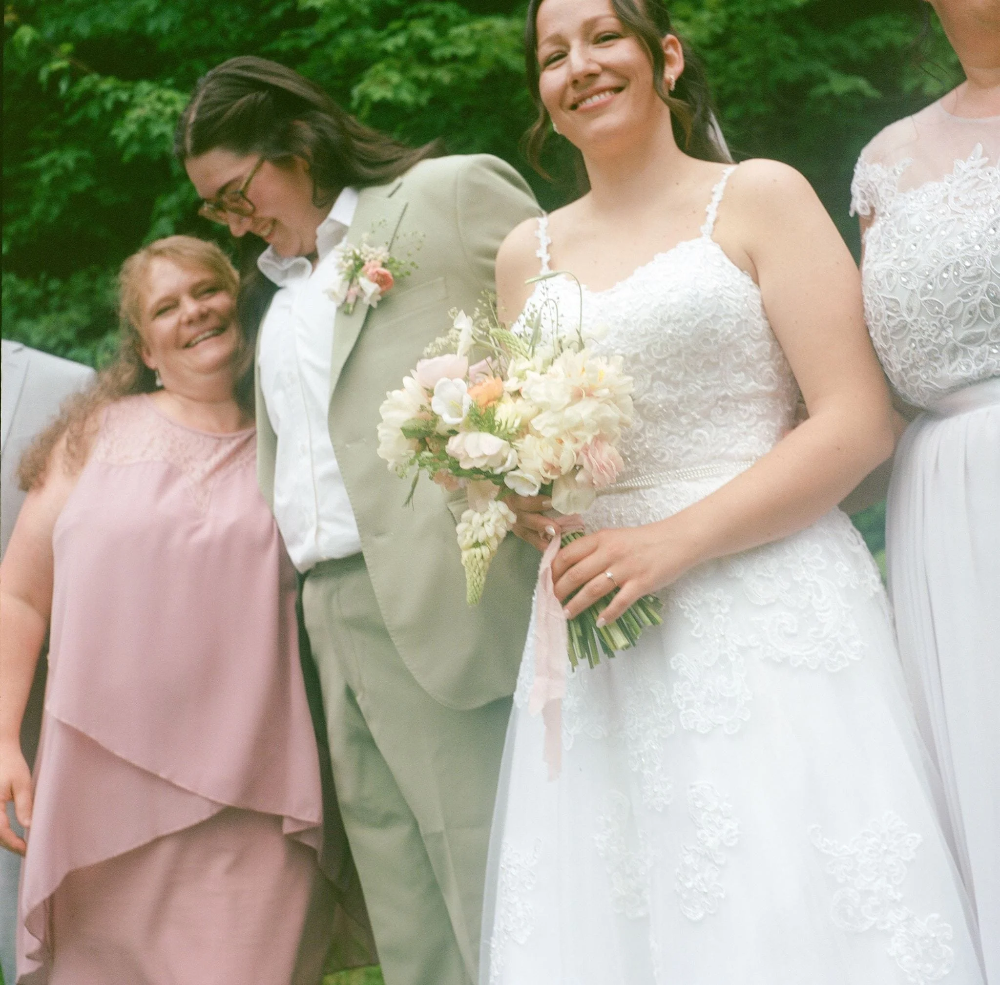 Groupe de femmes lors d'une célébration en plein air, avec deux femmes en robe de mariée, tenant un bouquet de fleurs, entourées d'autres femmes.