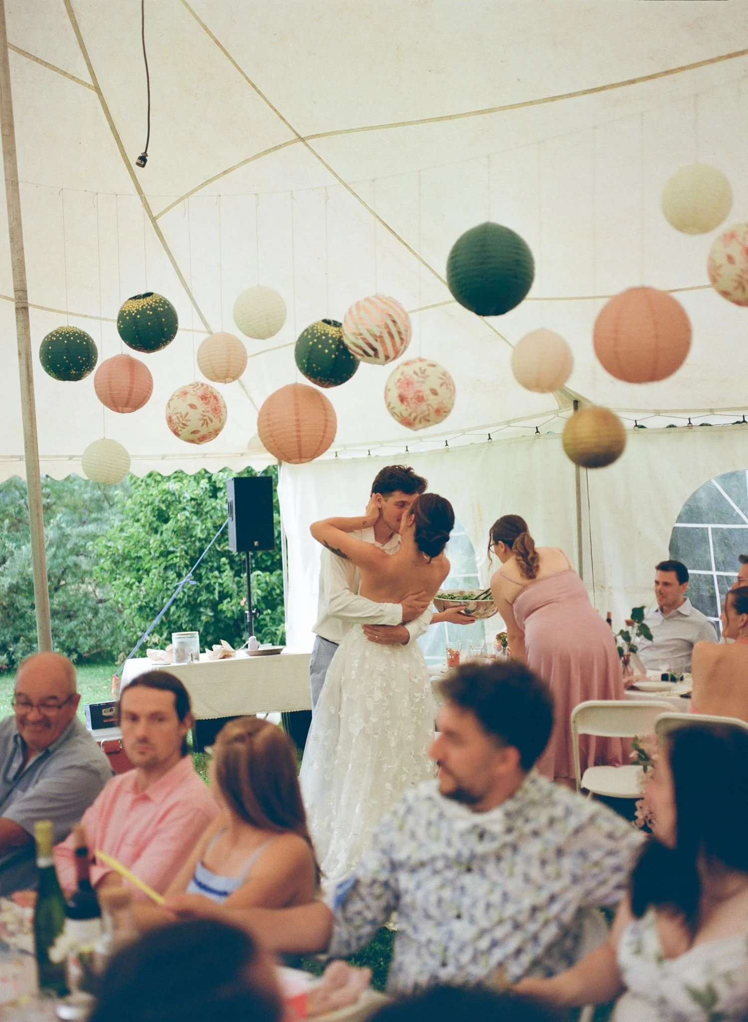Un groupe de personnes lors d'une célébration ou réception sous une tente, avec des décorations lumineuses suspendues au plafond, incluant des lanternes en papier de différentes couleurs et motifs, et des invités assis ou en train de se détendre auto