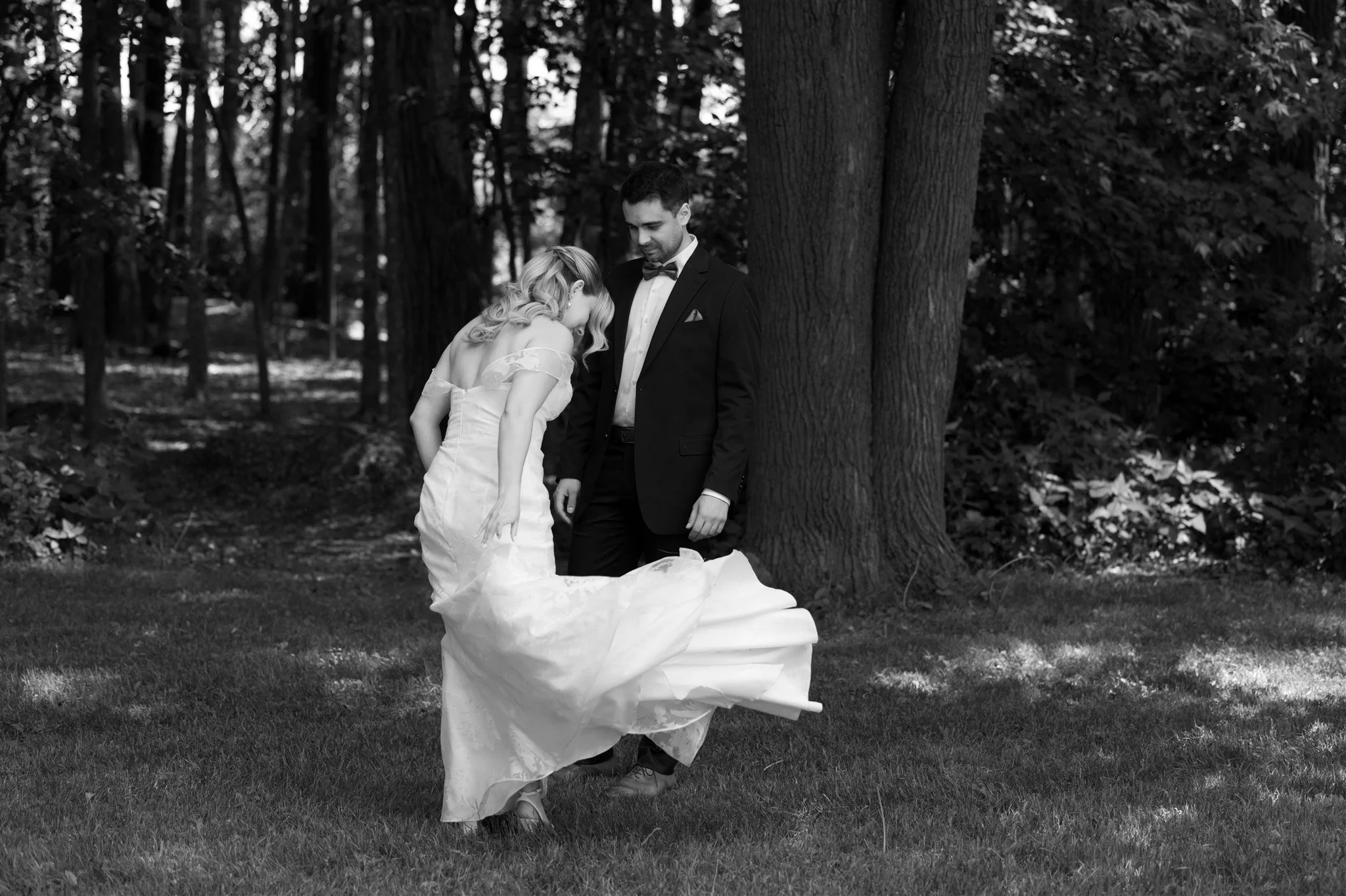 Un couple de mariés dans un parc, la femme portant une robe de mariée blanche et le homme en costume noir, souriant et partageant un moment de bonheur.