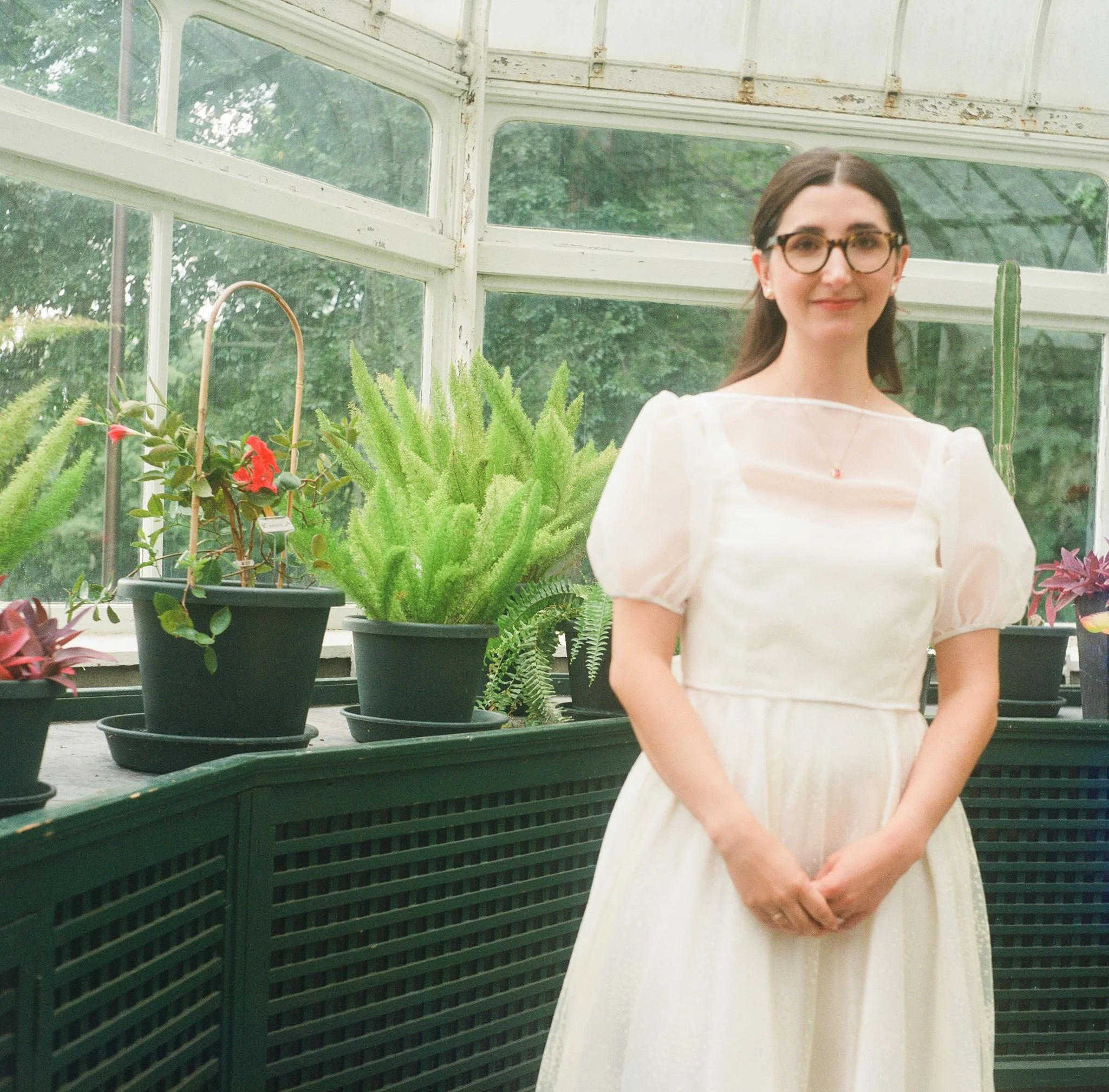 Femme portant une robe blanche dans une serre avec des plants de plantes en pot.