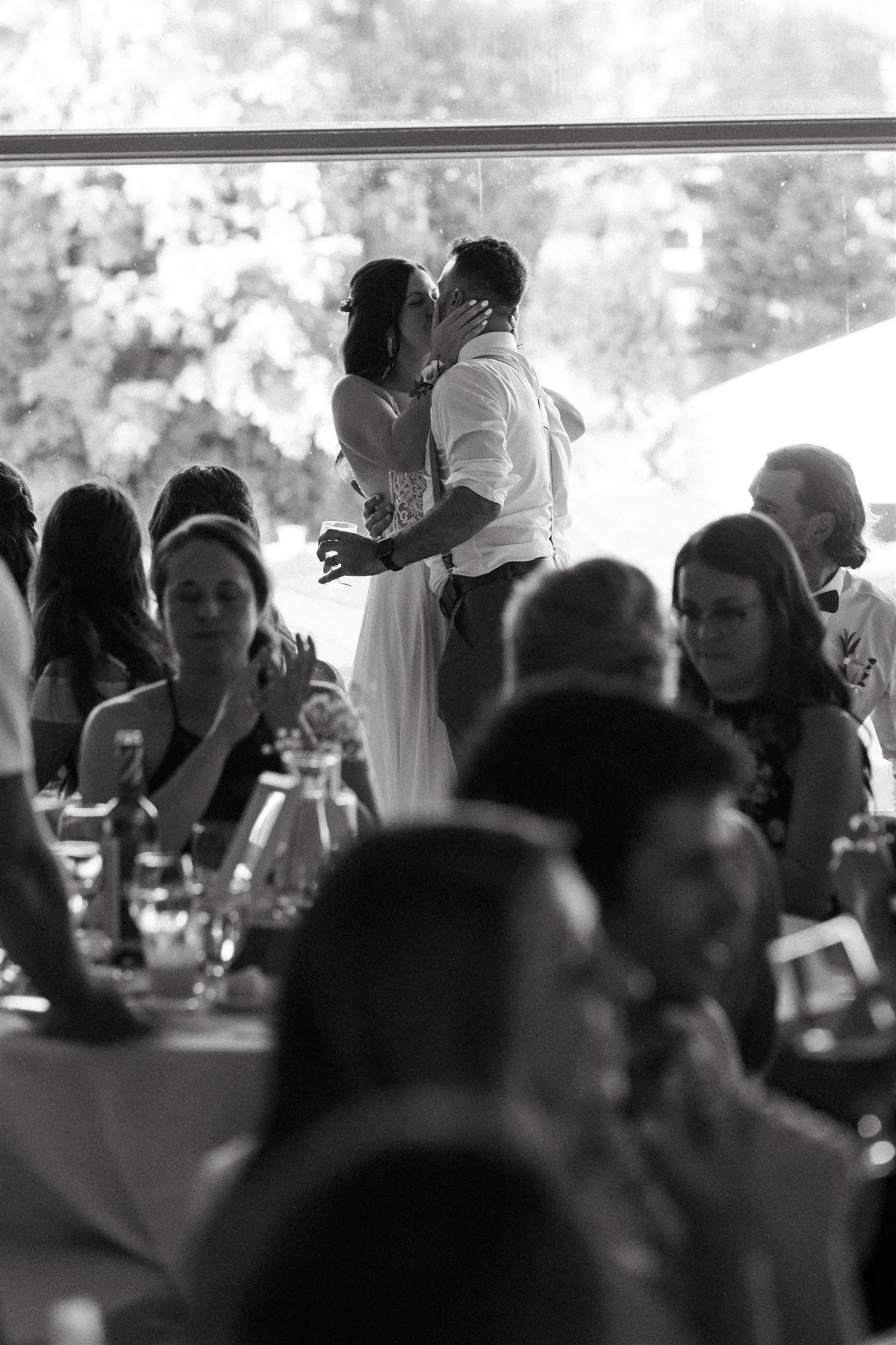 Un couple s'embrasse tendrement lors d'une cérémonie de mariage, entouré d'invités assis à une table.