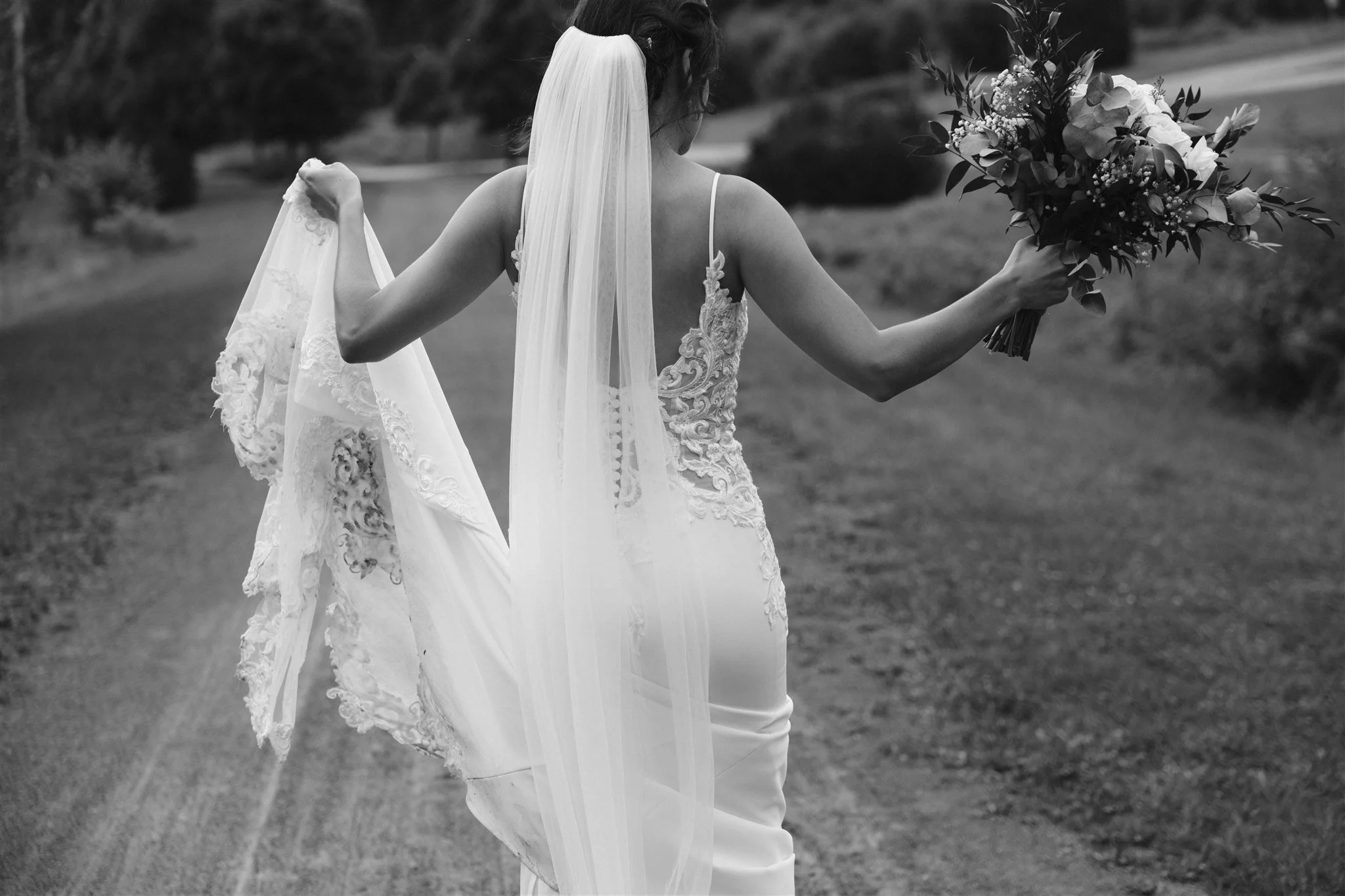Une femme en robe de mariée blanche tient un bouquet de fleurs et marche dans un espace extérieur herbeux.