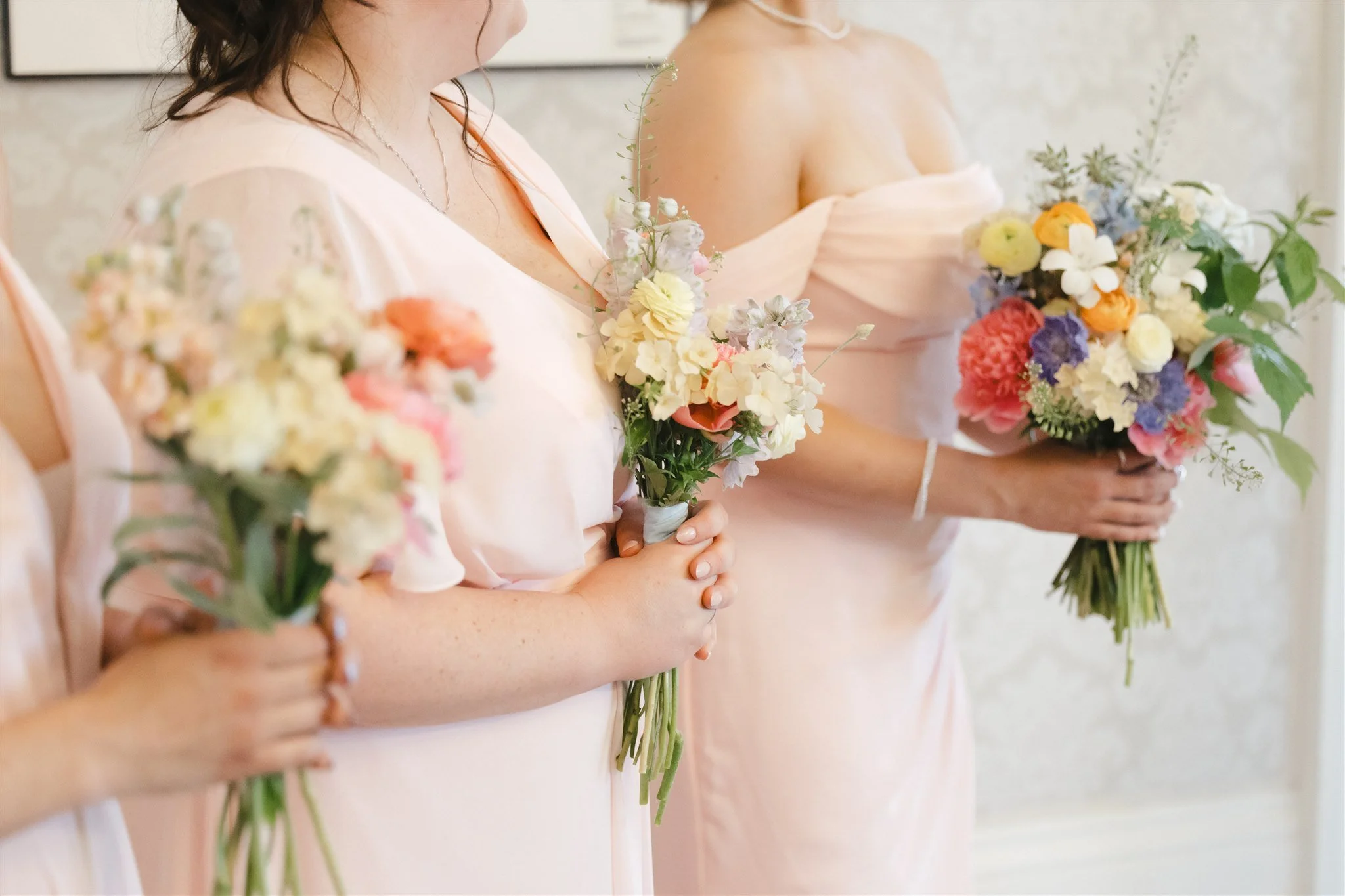 Groupe de femmes portant des robes pastel et tenant des bouquets de fleurs colorées lors d'une célébration.