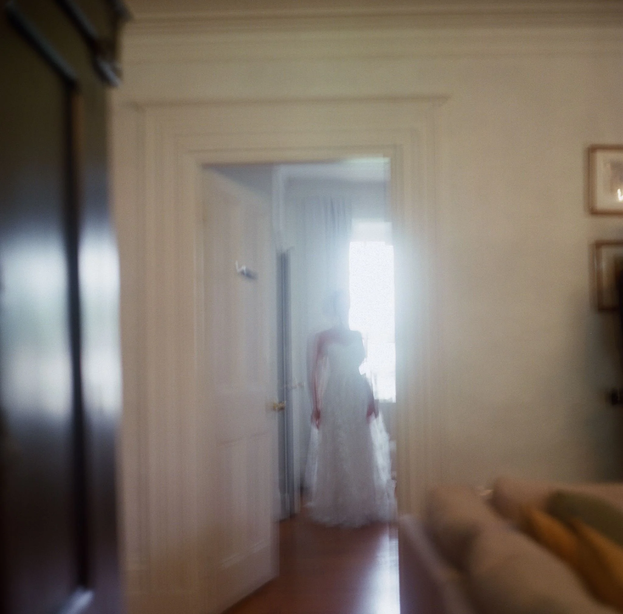 Un couloir dans une maison vue de l'intérieur, avec une porte ouverte à l'arrière-plan et des cadres accrochés au mur