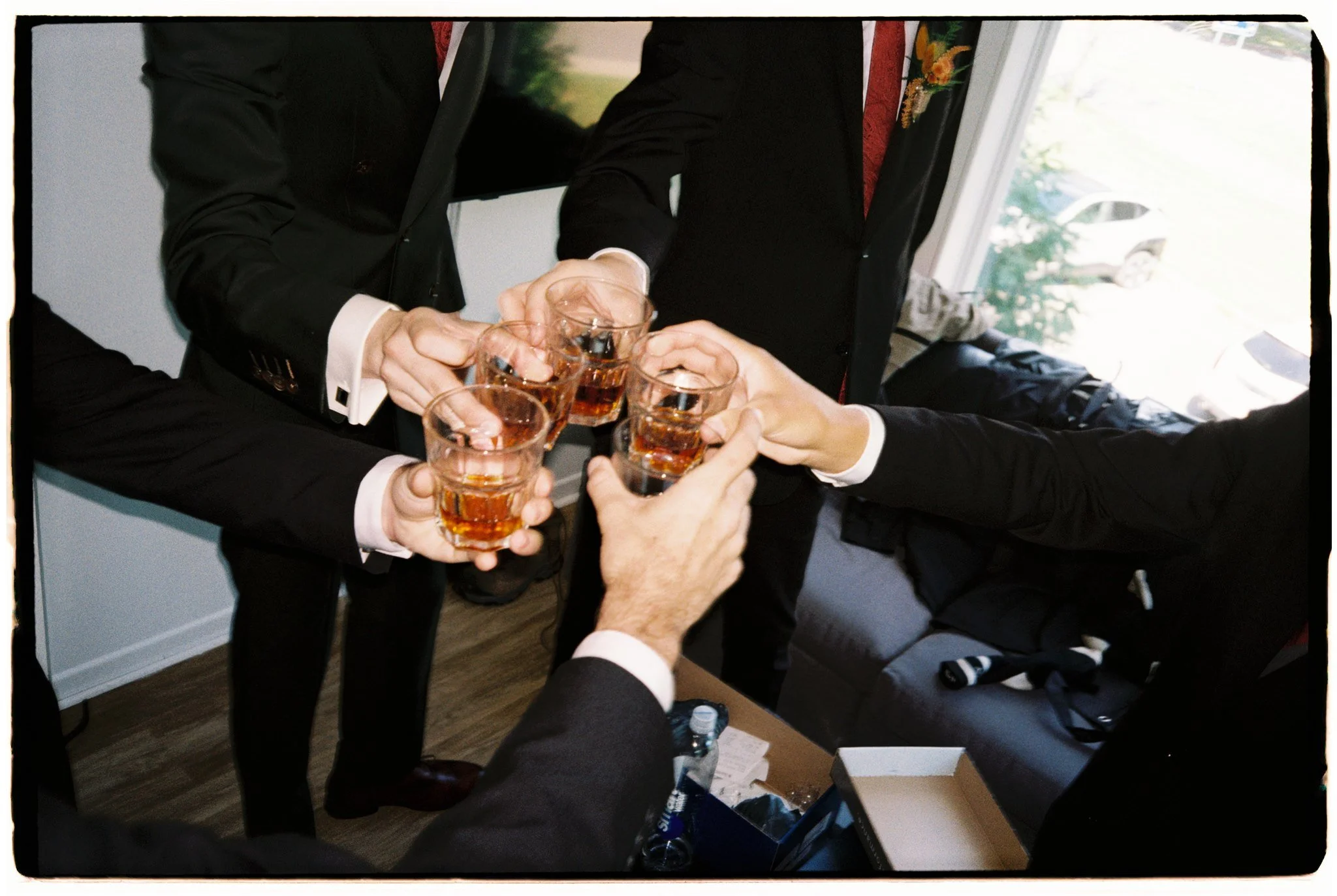 Groupe de personnes déguisées en costumes formels, en train de porter un toast avec des verres remplis d'une boisson foncée, lors d'une célébration ou réunion.