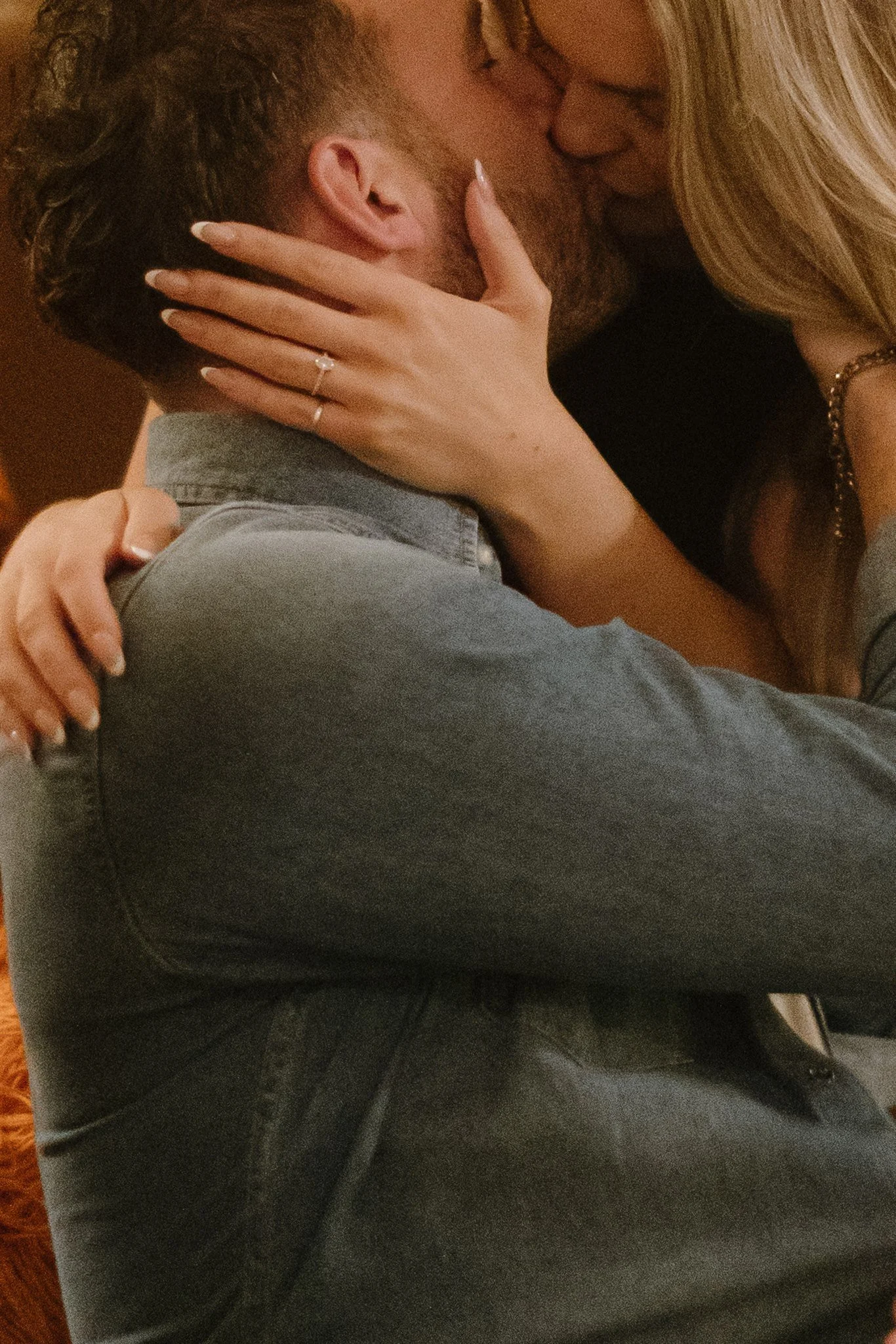 Un couple s'embrasse tendrement en position assise, avec la femme tenant le visage de l'homme avec ses mains. La femme porte une bague et un bracelet, et a des cheveux longs blonds. L'homme a les cheveux courts et foncés.