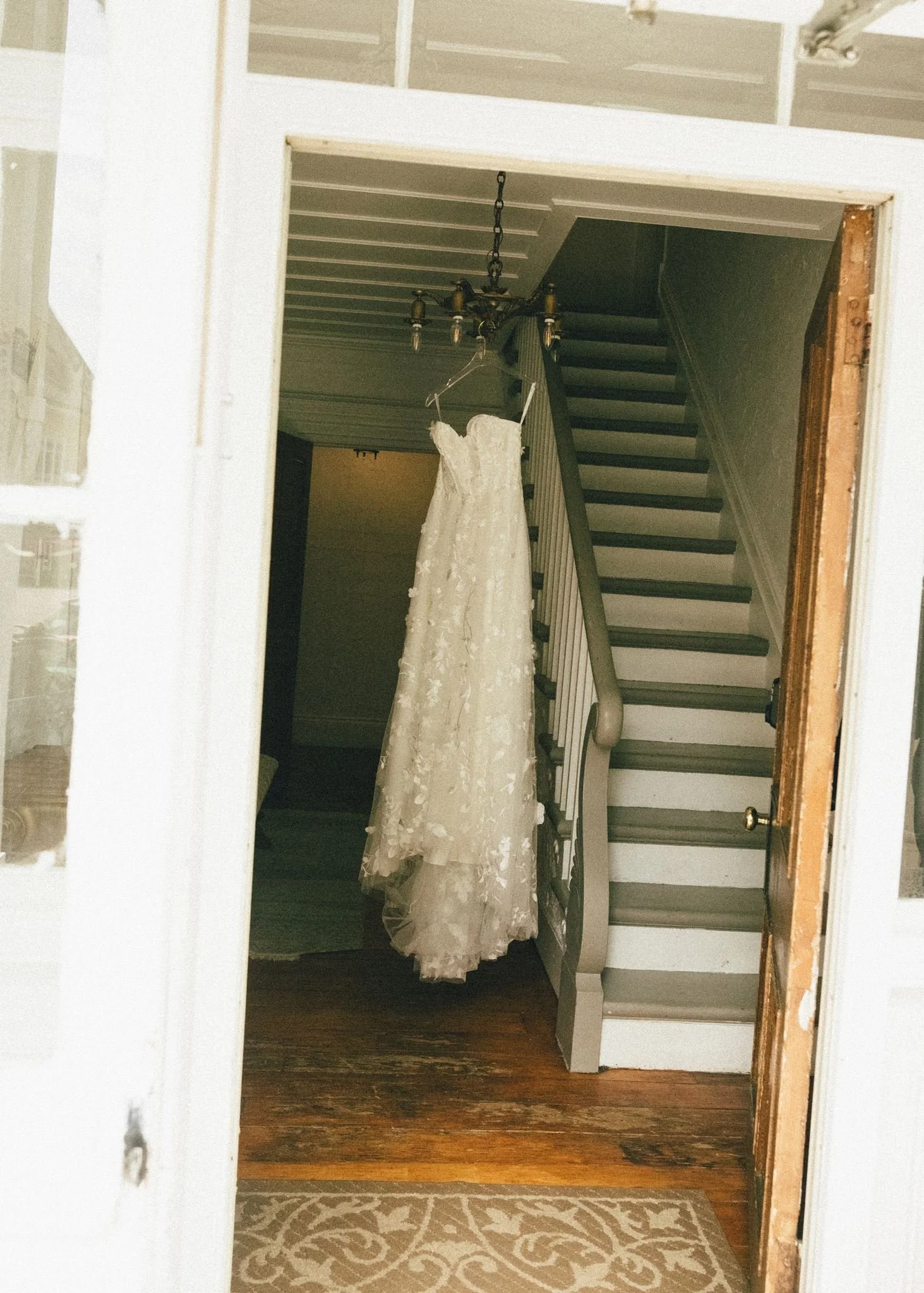 Une robe de mariée blanche suspendue dans un couloir avec un escalier en arrière-plan.
