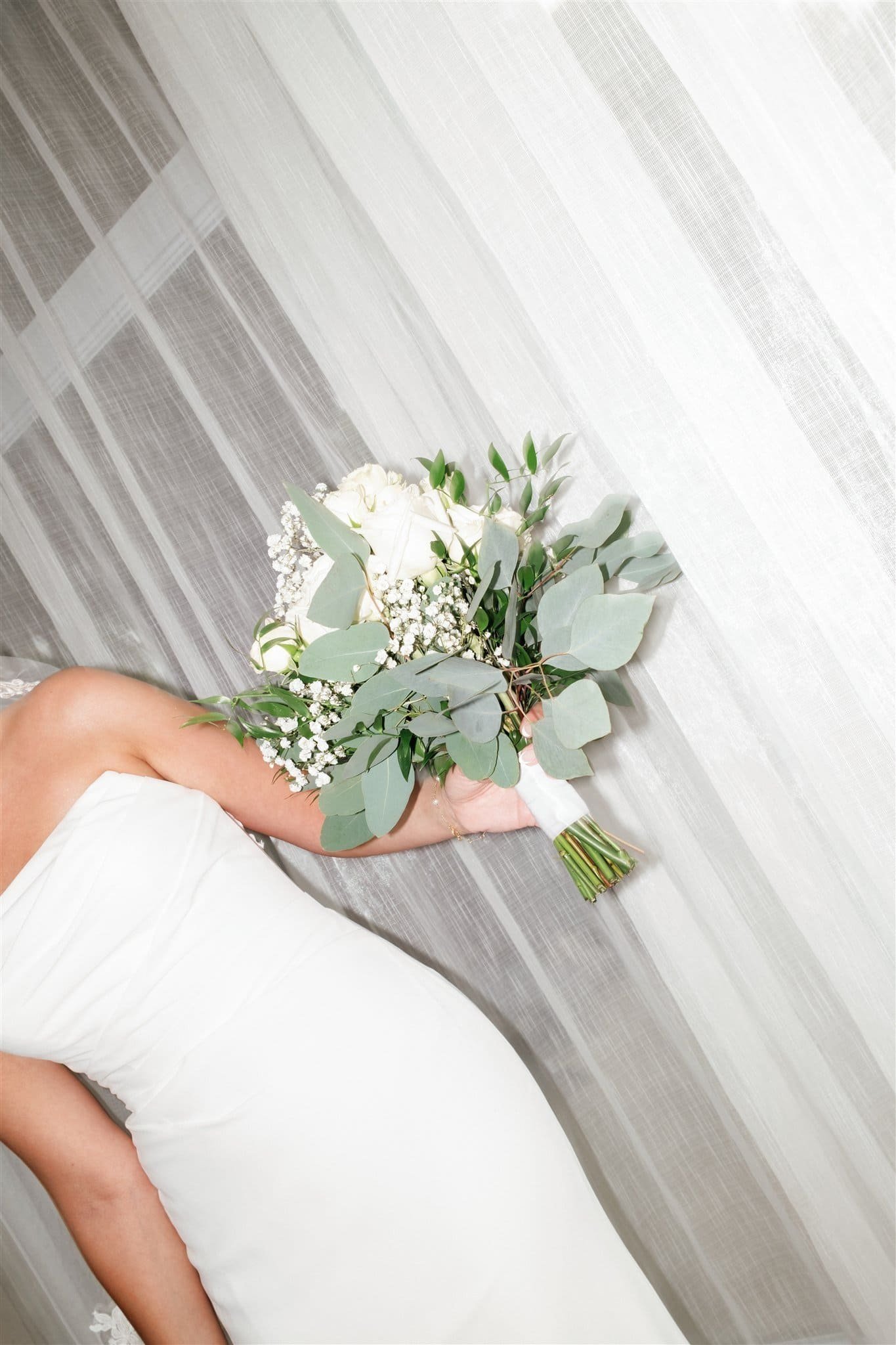 Bouquet de mariage composé de roses blanches, gypsophile et eucalyptus, tenu par une personne en robe blanche, capté par un Photographe mariage Québec dans une chambre à Entourage sur le Lac.