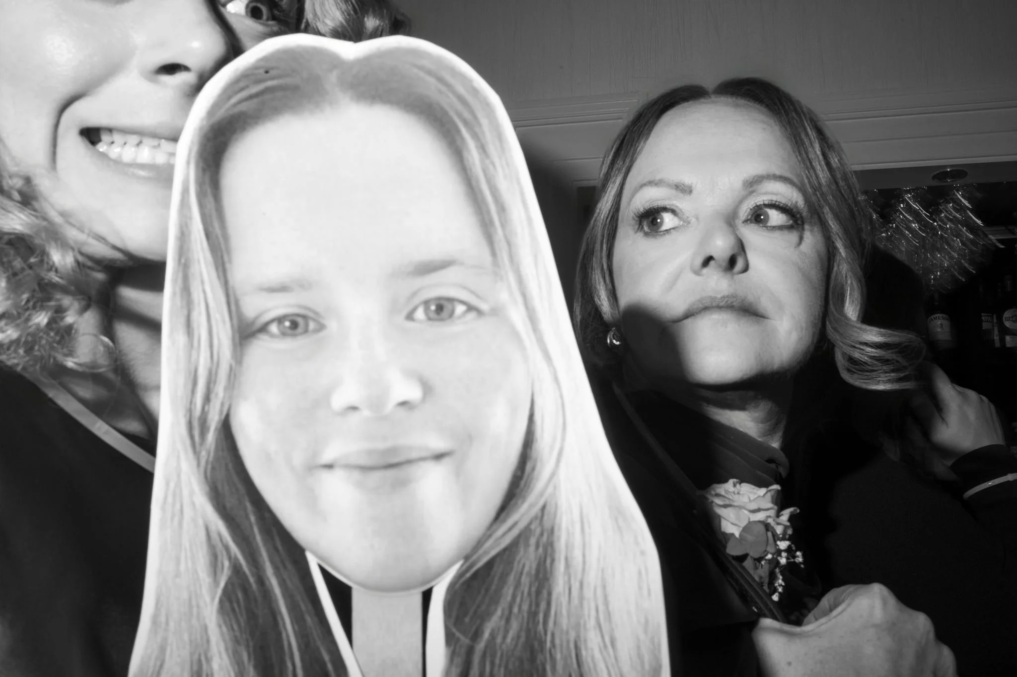 Photo en noir et blanc de plusieurs personnes, dont certaines portent des masques avec des visages d'enfants et une femme regarde vers la droite.
