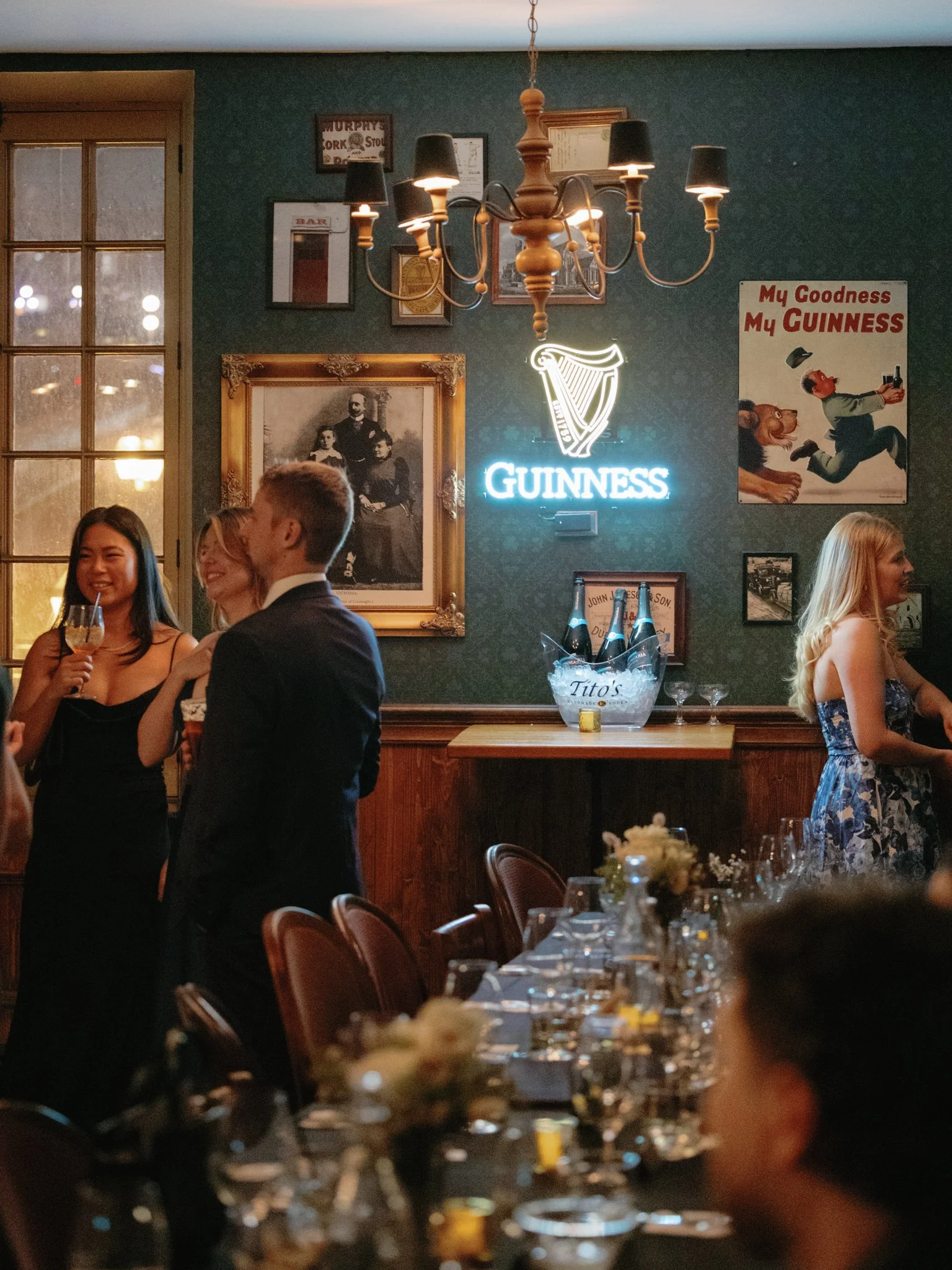 Groupe de personnes élégantes célébrant dans un pub irlandais à l’ambiance chaleureuse, décor antique, néon Guinness et affiches vintage, capté par un photographe mariage Québec Montréal.