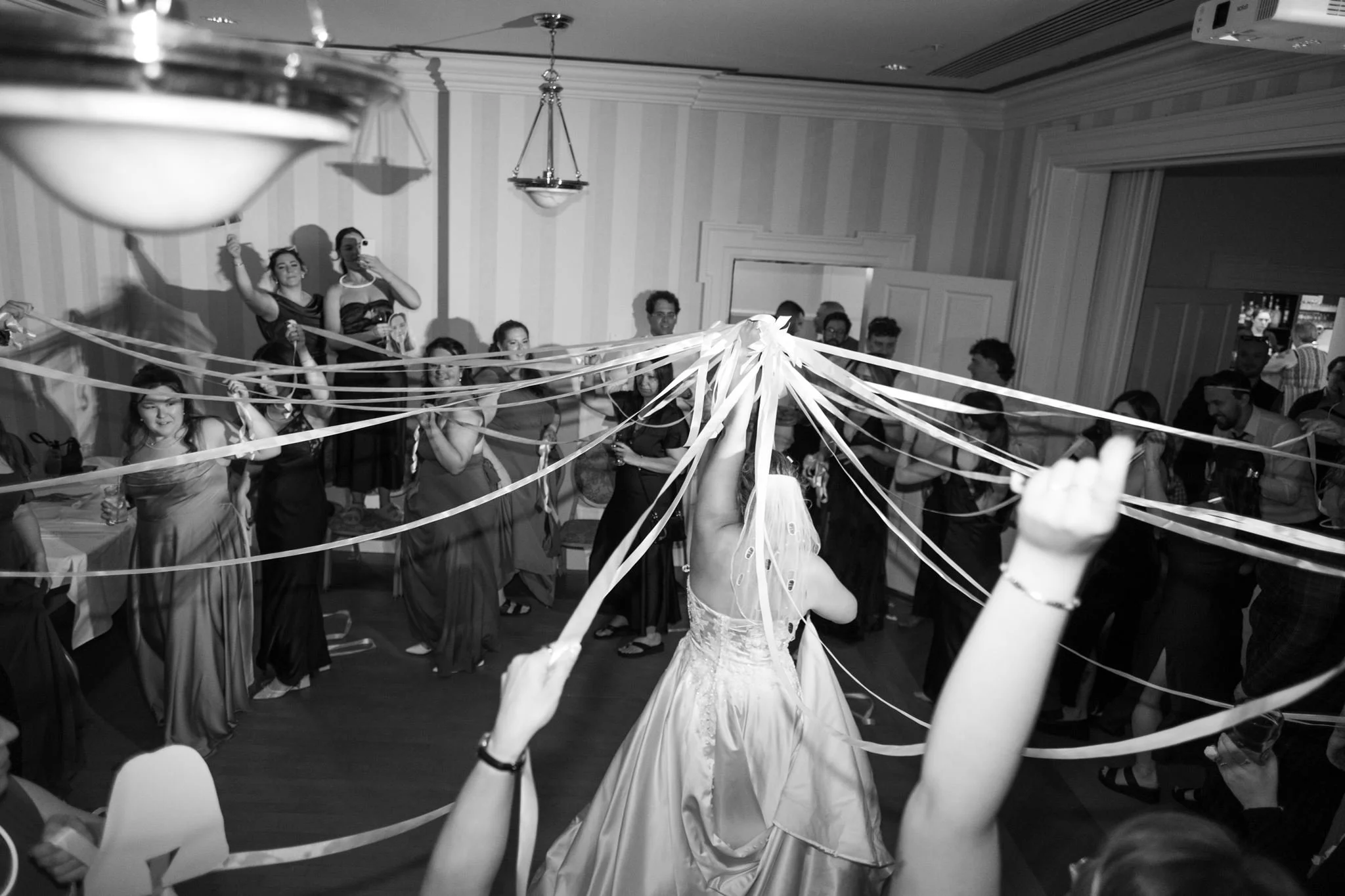 Une scène de mariage avec des invités entourant la mariée, décorée avec des rubans blancs suspendus au plafond.