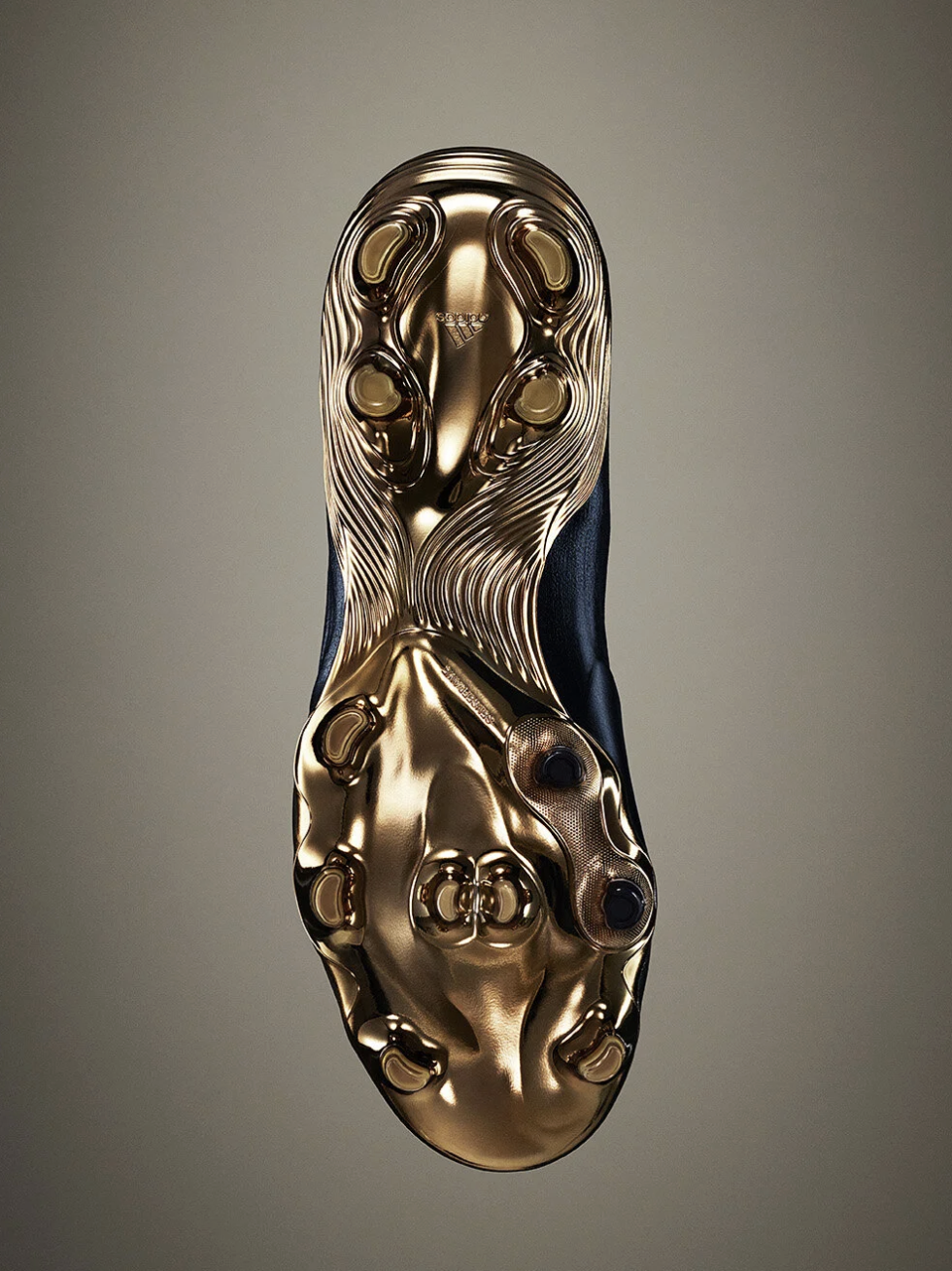 A close-up view of the sole of an Adidas soccer cleat, featuring gold-colored studs and a sleek black and gold design.