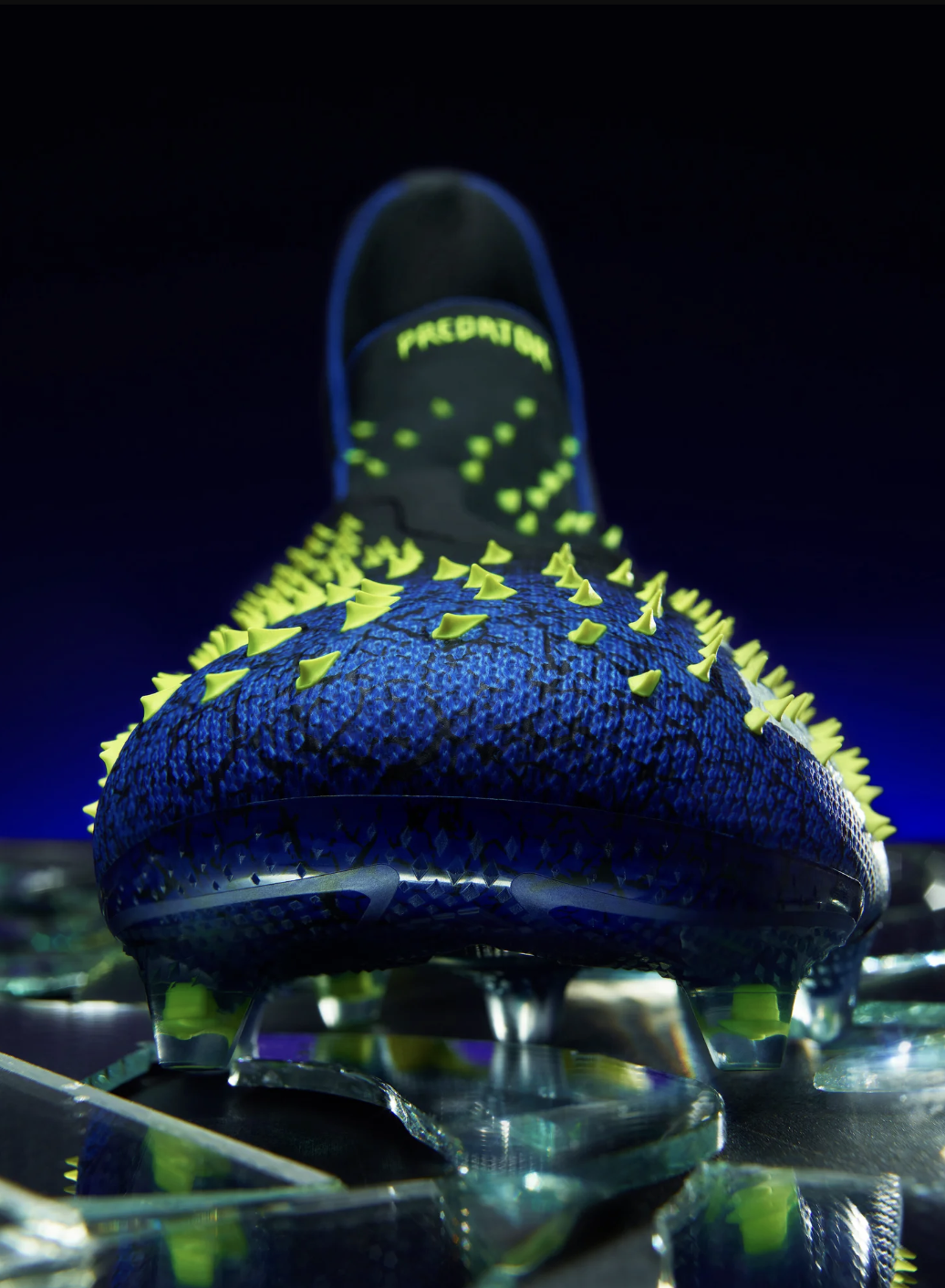 Close-up of a Futuristic Adidas Predator soccer shoe with neon green spikes and accents, highlighted under blacklight, with a reflective surface.