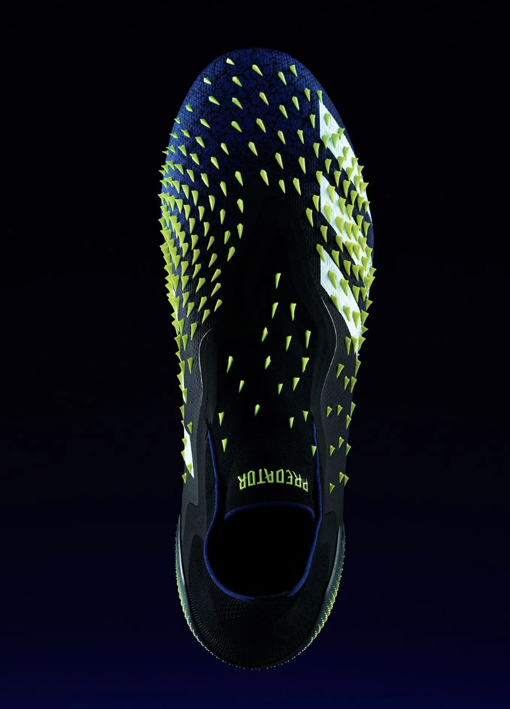 A black and neon green running shoe with spike studs, displayed against a dark background, with the word "PREDATOR" on the insole.