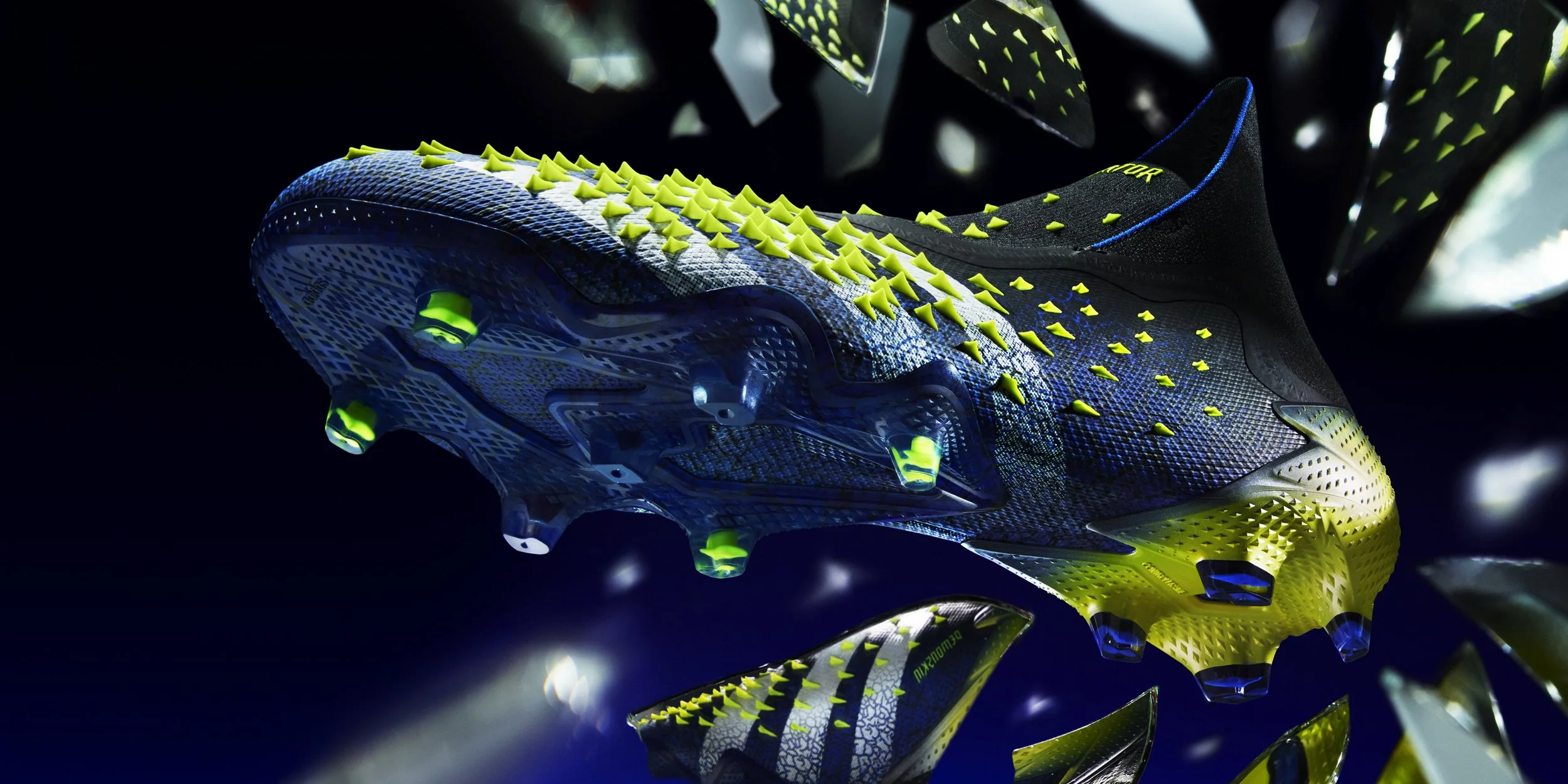 Close-up of a futuristic athletic shoe with vibrant yellow and blue spikes on a dark background, with glass fragments reflecting the shoe.