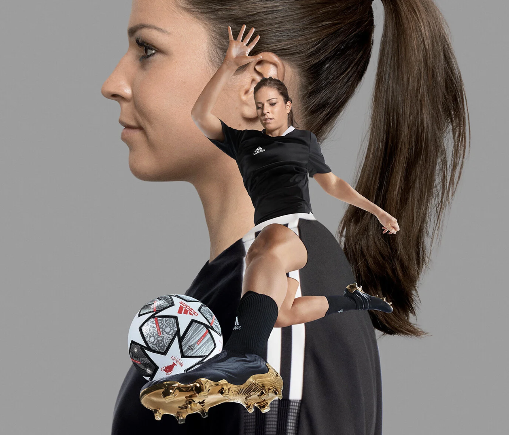 A female soccer player in black uniform with white accents, wearing black cleats and knee-high socks, jumping with her right knee raised during a match. She is balancing her left foot on a professional Adidas soccer ball with a white, black, and red geometric design and gold studs underneath, which is suspended in mid-air. The background features a large, semi-transparent image of a woman's face with long brown hair, in profile, against a plain gray backdrop.