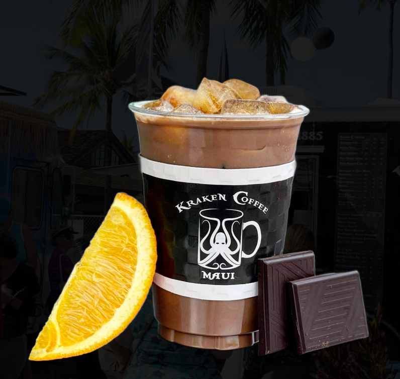 Cold iced mocha coffee with ice cubes in a plastic cup with a 'Kraken Coffee Maui' logo, garnished with an orange wedge and two pieces of dark chocolate, set against a tropical background with palm trees.