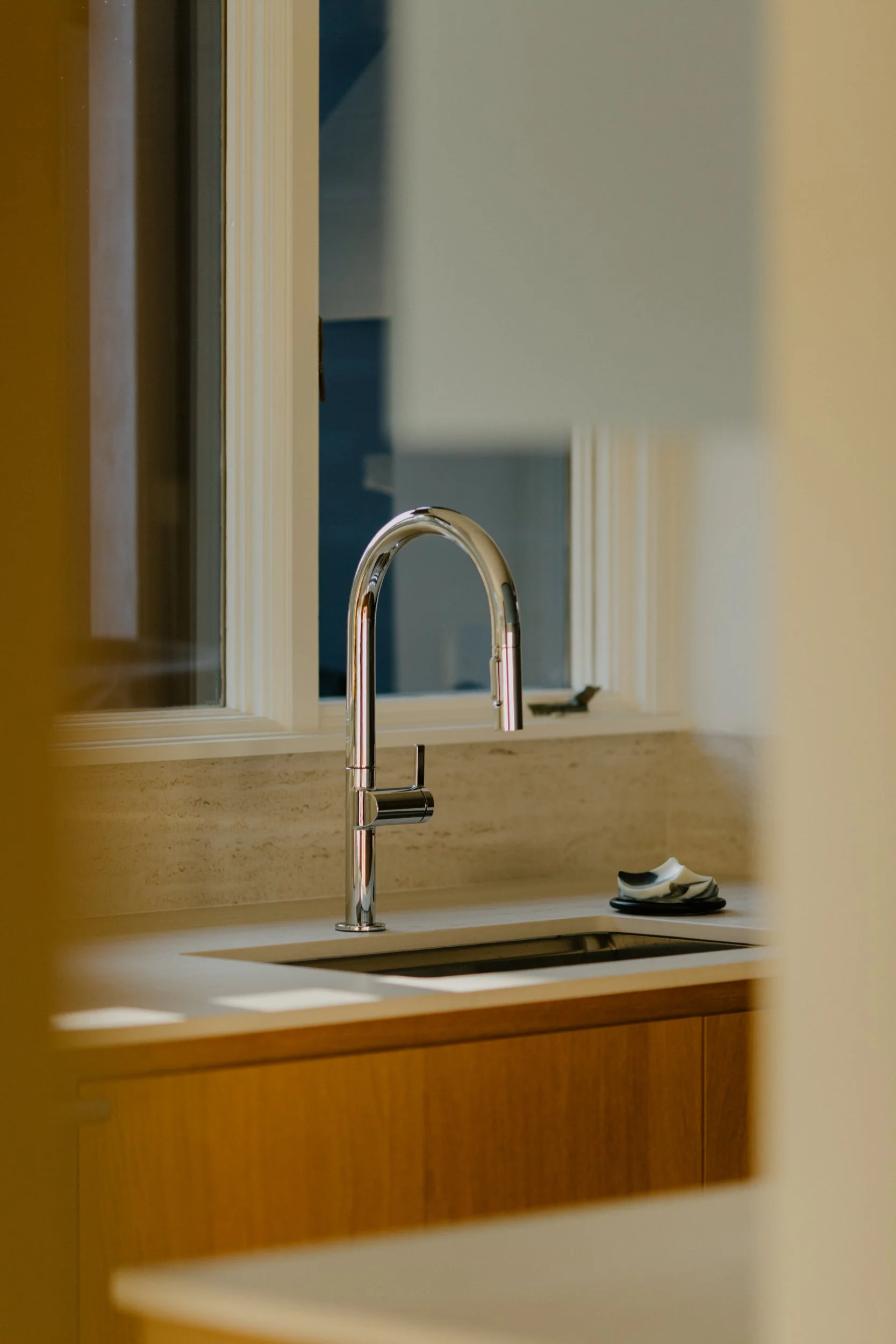 A kitchen sink with a chrome faucet, a window above the sink, and a few small objects on the right side of the counter.