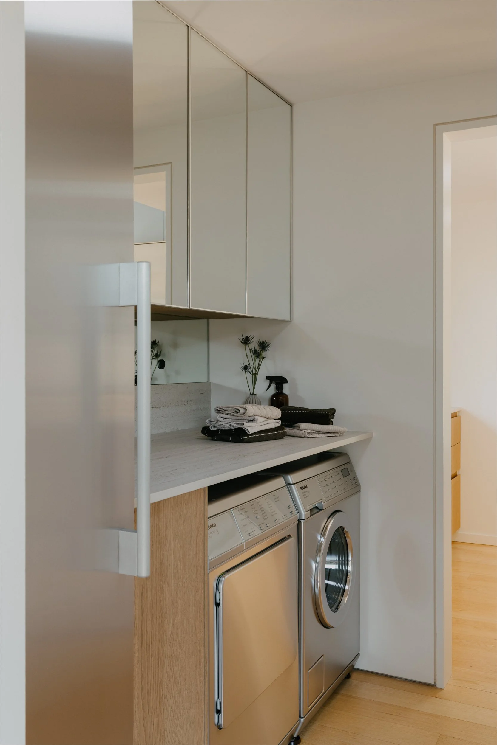 Laundry room with washing machine, dryer, white cabinets, and countertop with neatly folded towels, a spray bottle, and flowers in a vase.