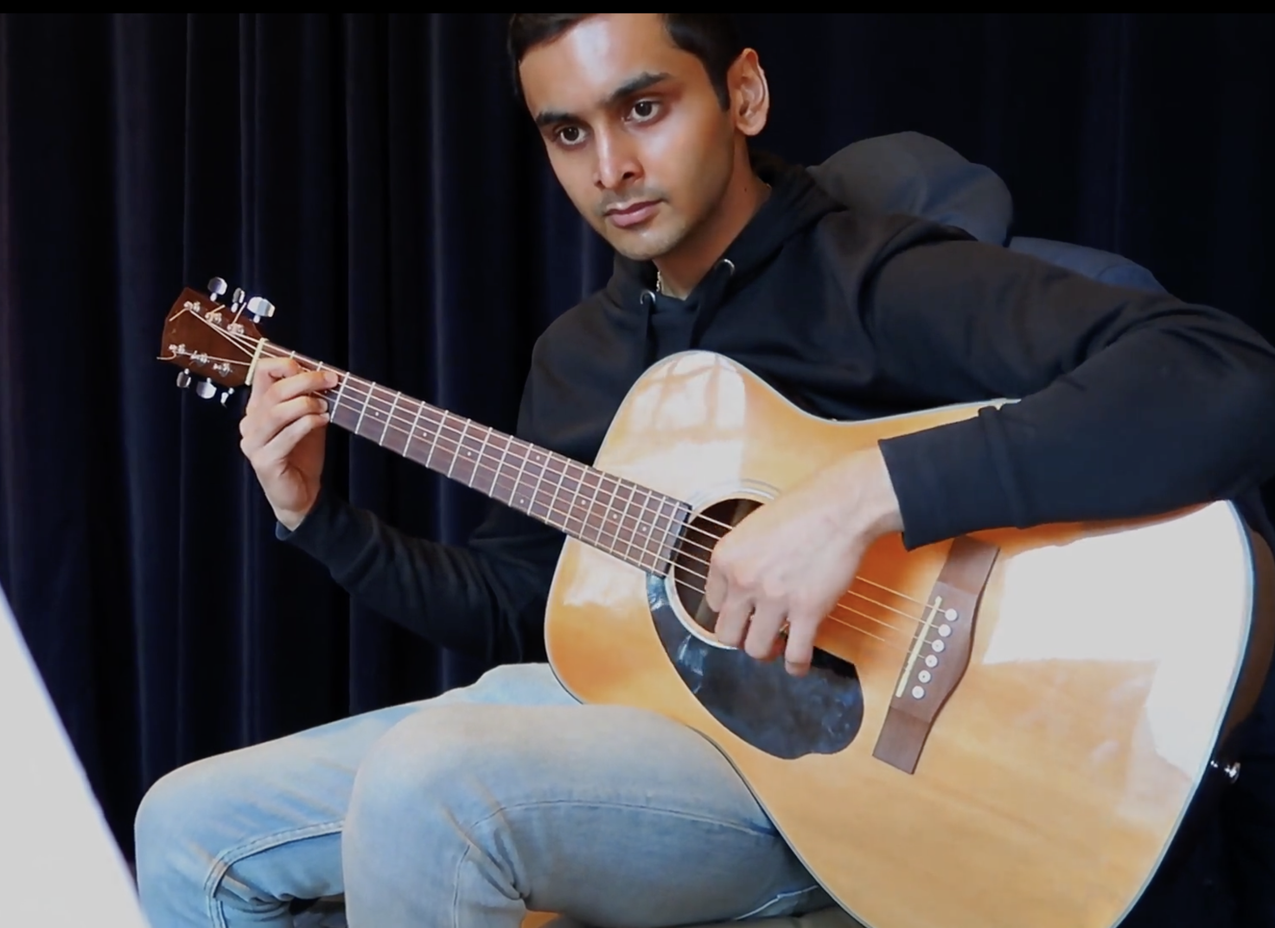 Jeune homme jouant de la guitare acoustique devant un fond de rideau noir.