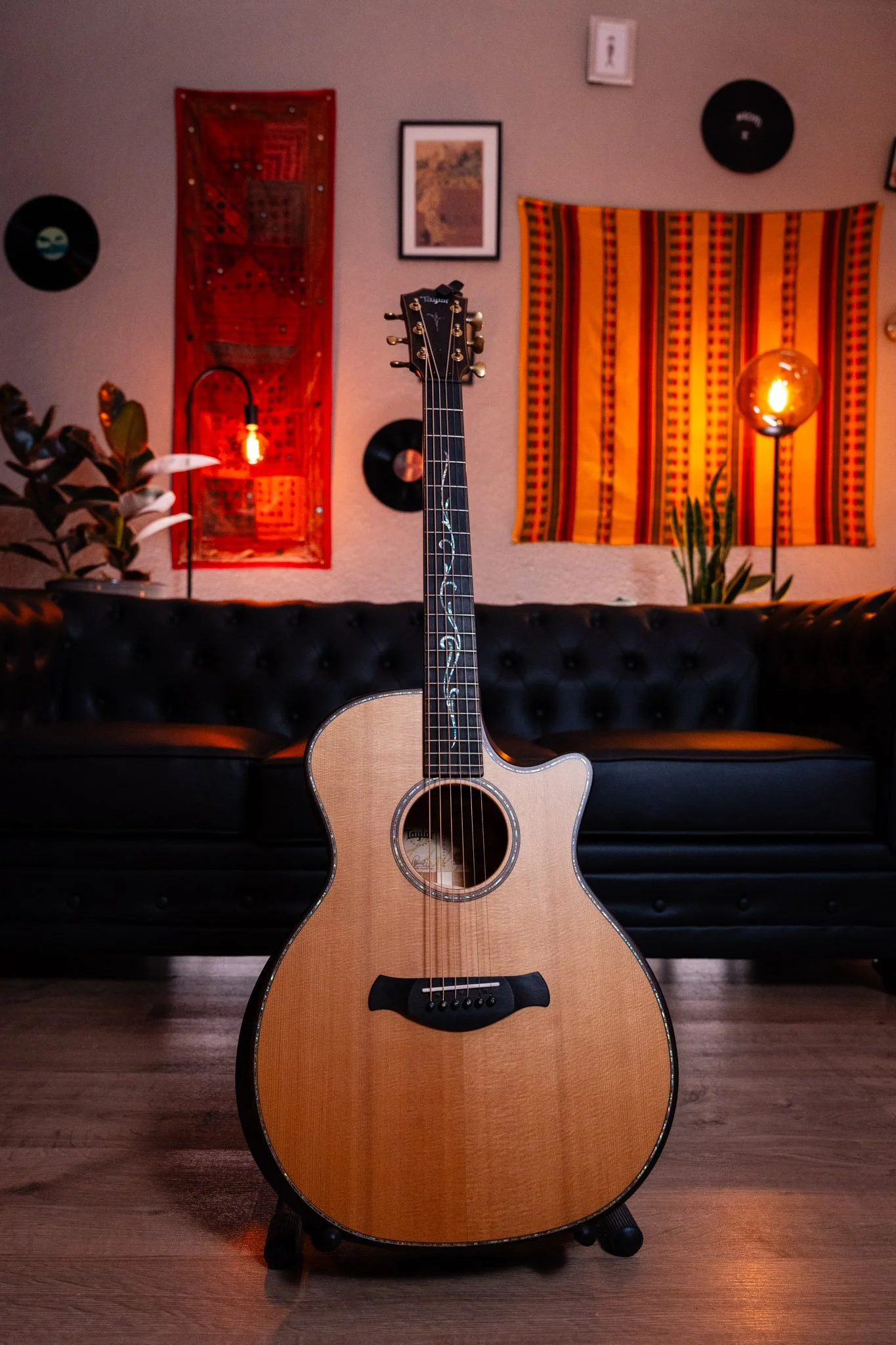 Guitare acoustique en bois clair positionnée au centre d'une pièce décorée avec des affiches, des tapis tissés et des lampes chaleureuses.