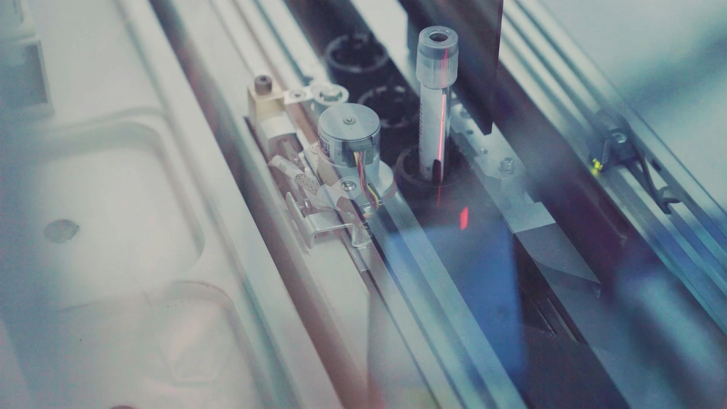 Close-up view of a scientific instrument with metal components, circuit wires, and glass tube inside a machine or laboratory setting.
