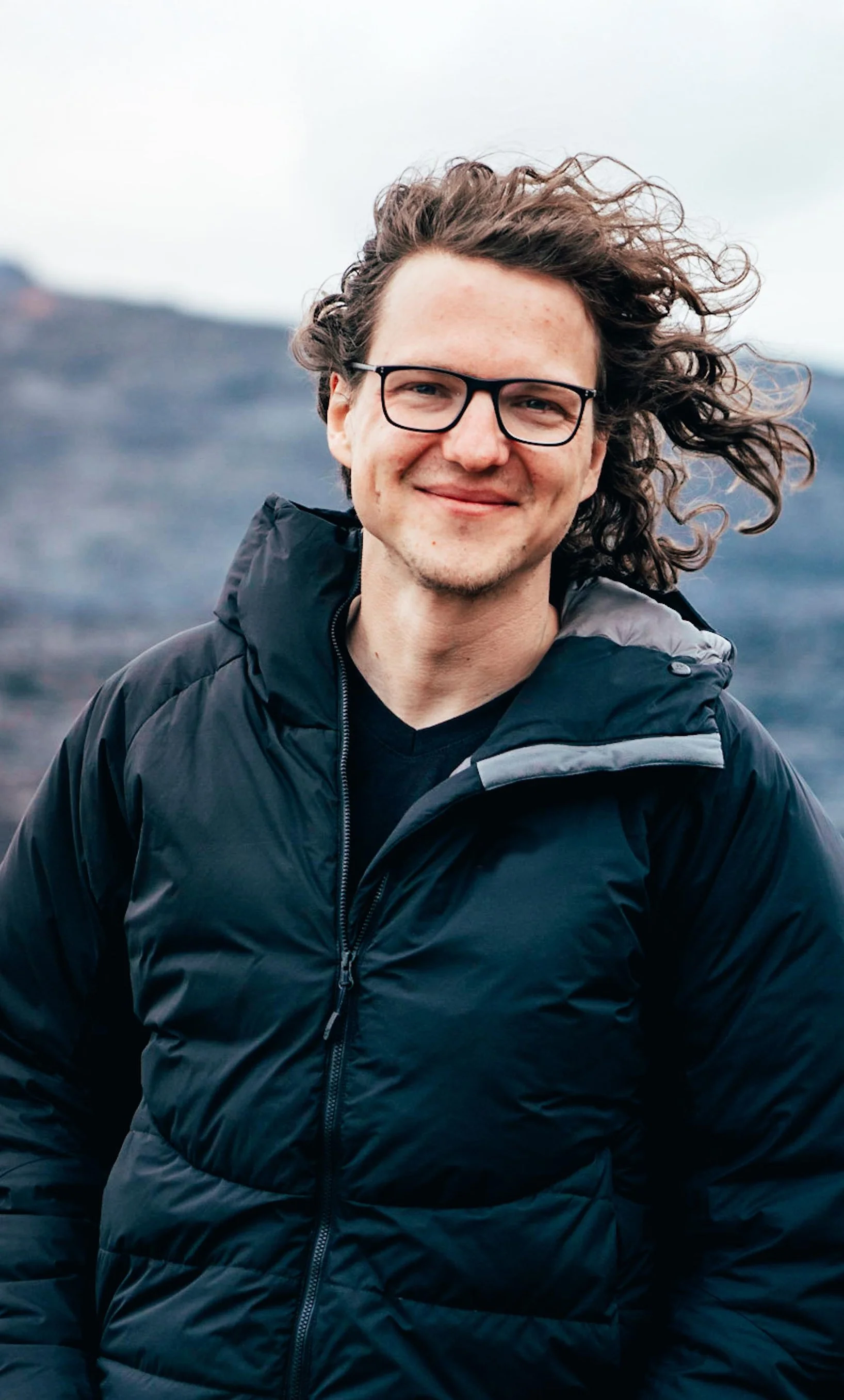 Niklas Hlawatsch steht im freien vor einem Berg und lächelt in die Kamera