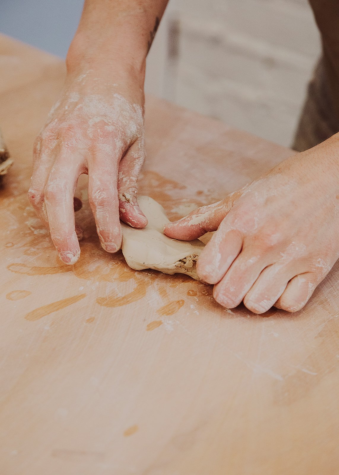 Close-up of potter's hands wedging clay on a wooden worktable at Still Life Ceramics Studio in Richmond, VA, captured by Fairy Bread Photography.