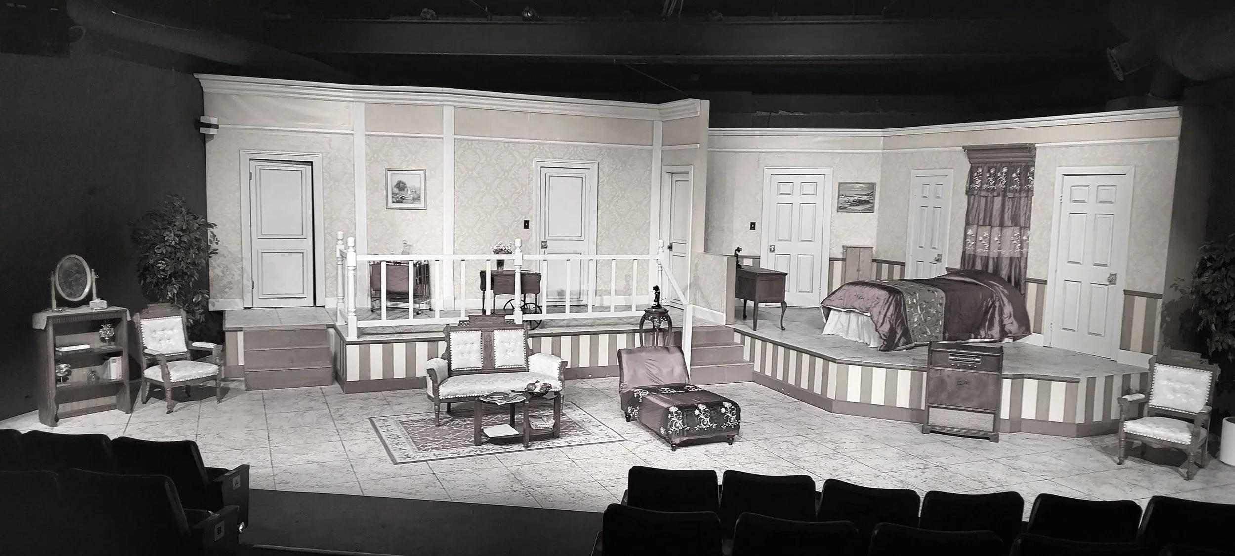 Stage set designed like a vintage bedroom with furniture, including a bed, chairs, a sofa, and decorative elements, in our black box theatre.